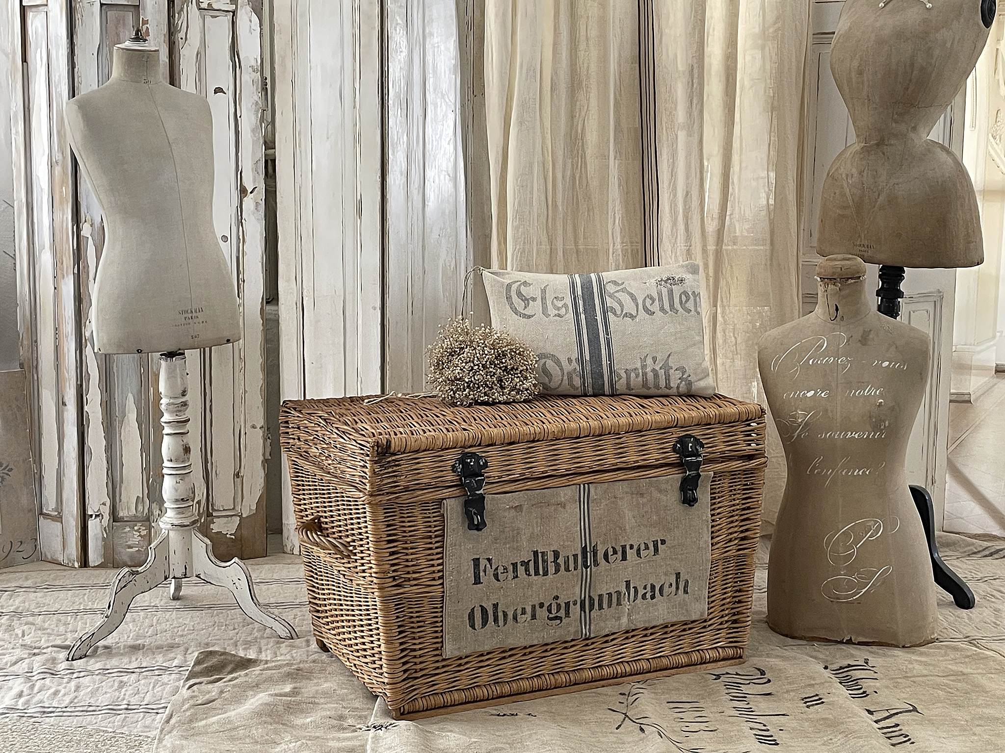Stilvolles Set mit Rattantruhe und Schneiderpuppen Dekoratives Bild mit einer Rattantruhe, Hintergrund mit Schneiderpuppen und vintage Stoffen.