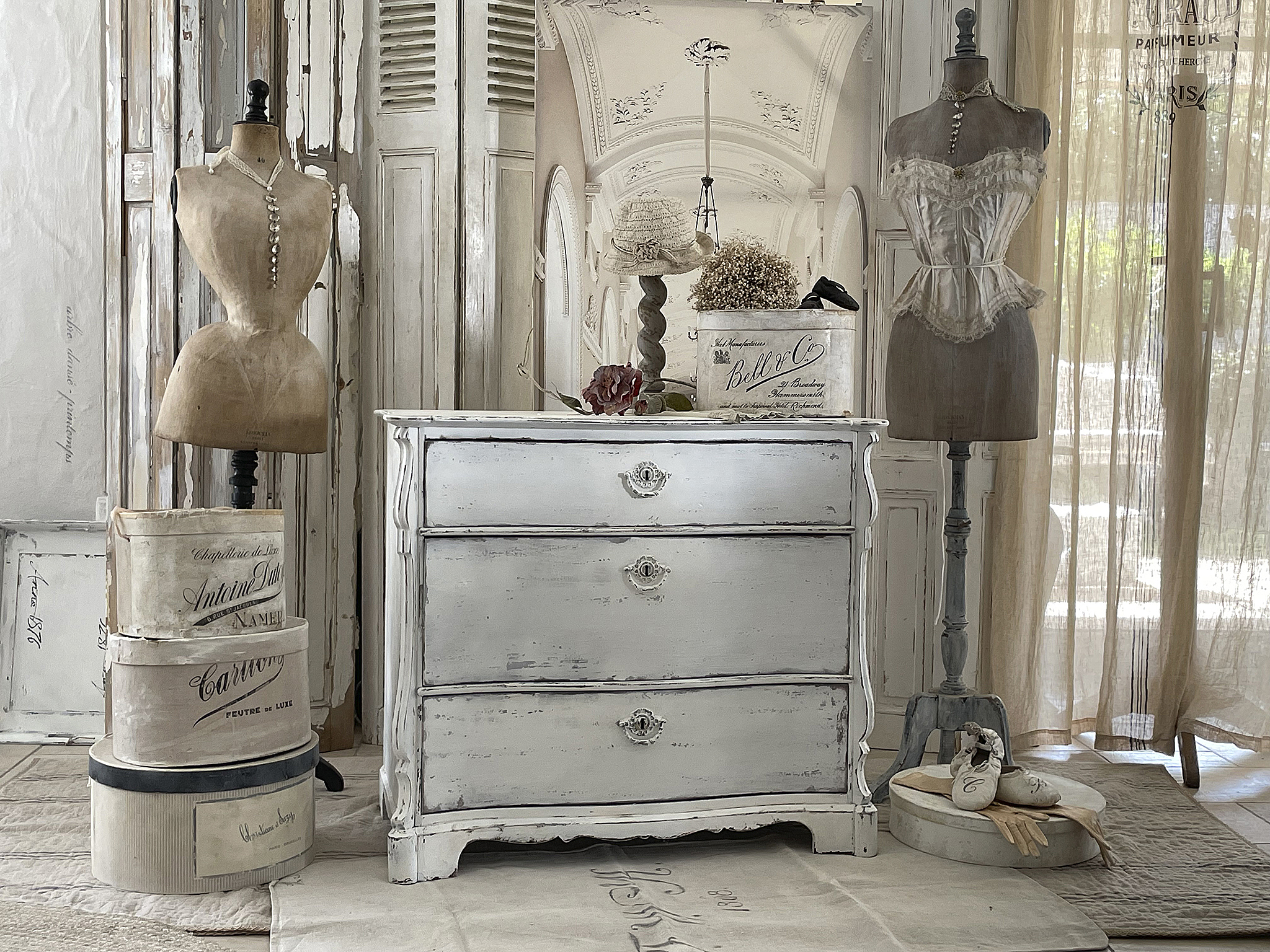 Antike Kommode in hellem Holz mit dekorativen Schneiderpuppen und vintage Aufbewahrungskisten in einem stilvollen Raum