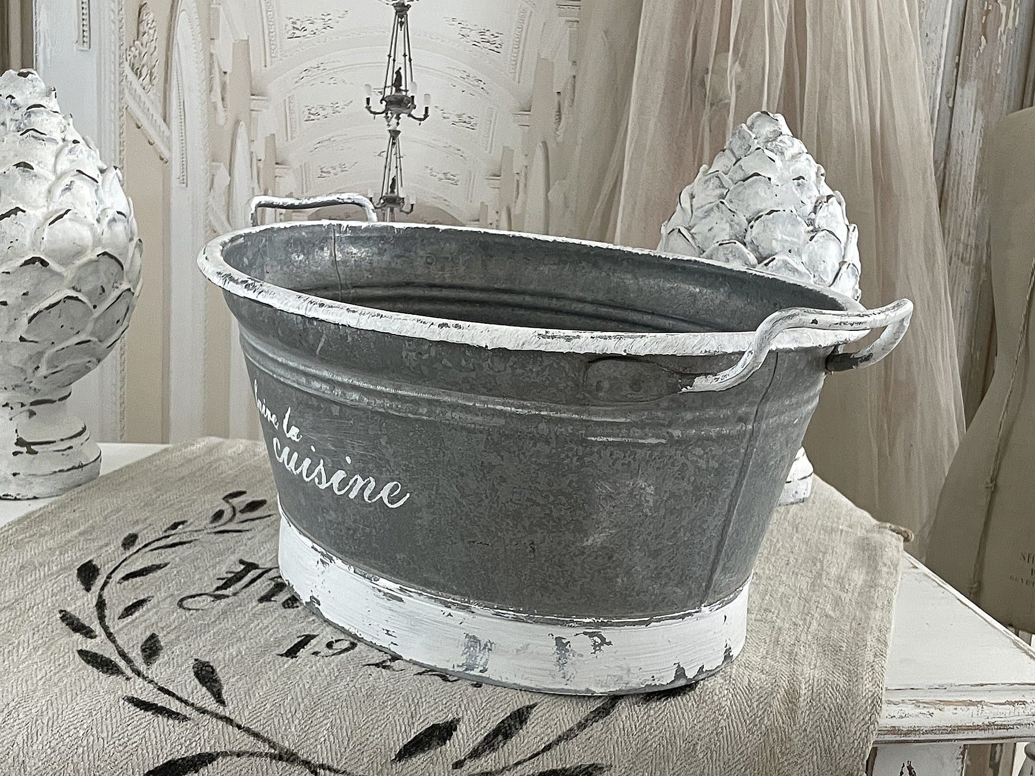 Dekorative Zinkwanne mit Aufschrift auf einem Tisch, umgeben von stilvollen Accessoires
