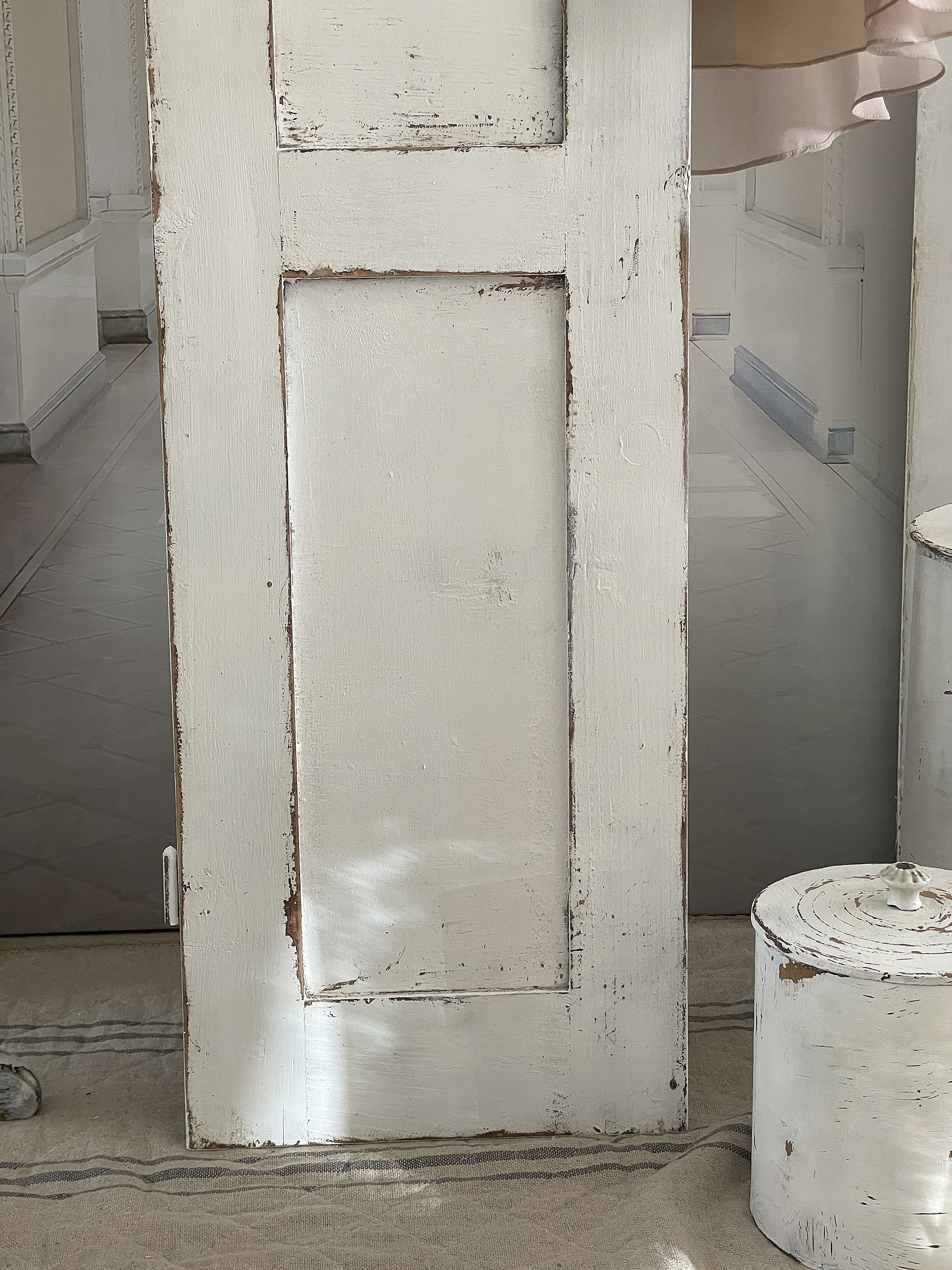 Weißer Vintage-Türrahmen mit Patina-Optik Nahaufnahme eines weißen Vintage-Türrahmens mit Abnutzungsspuren und einem runden weißen Behälter im Hintergrund.