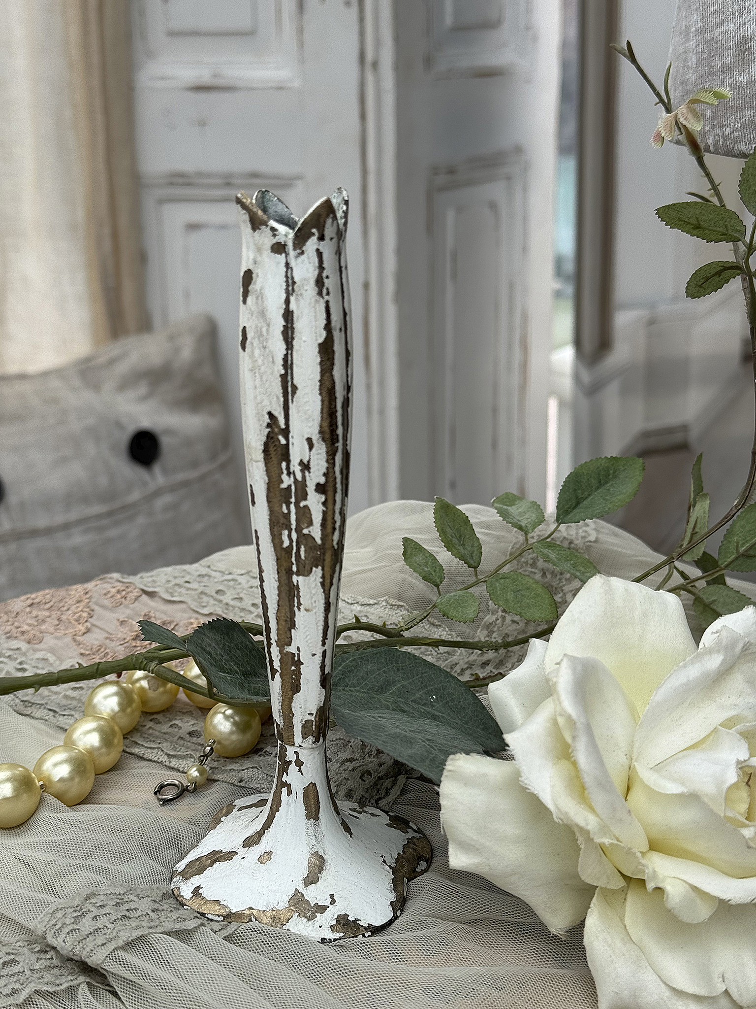 Dekorativer Vintage-Blumenständer aus Metall in Weiß und Gold Antiker Blumenständer aus Metall mit Patina, umgeben von einer weißen Rose und einer Perlenkette