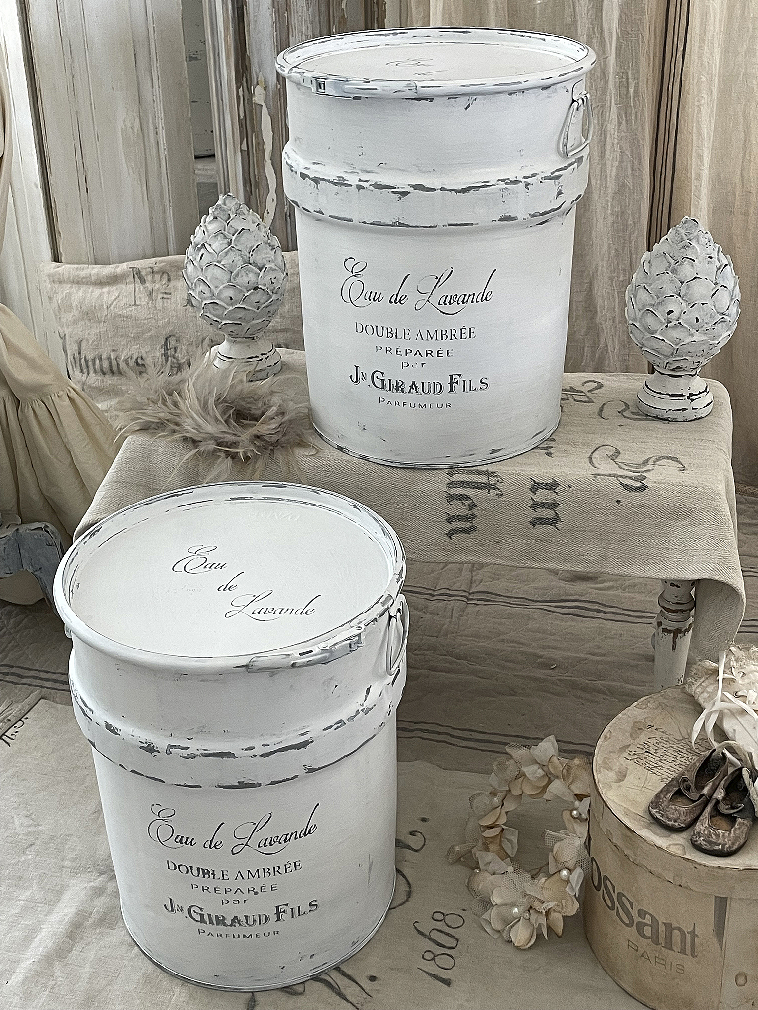 Dekorative weiße Duftbehälter mit Lavendel-Essenz Zwei dekorative weiße Eimer mit der Aufschrift Eau de Lavande, umgeben von stilvollen Accessoires und Dekoration.