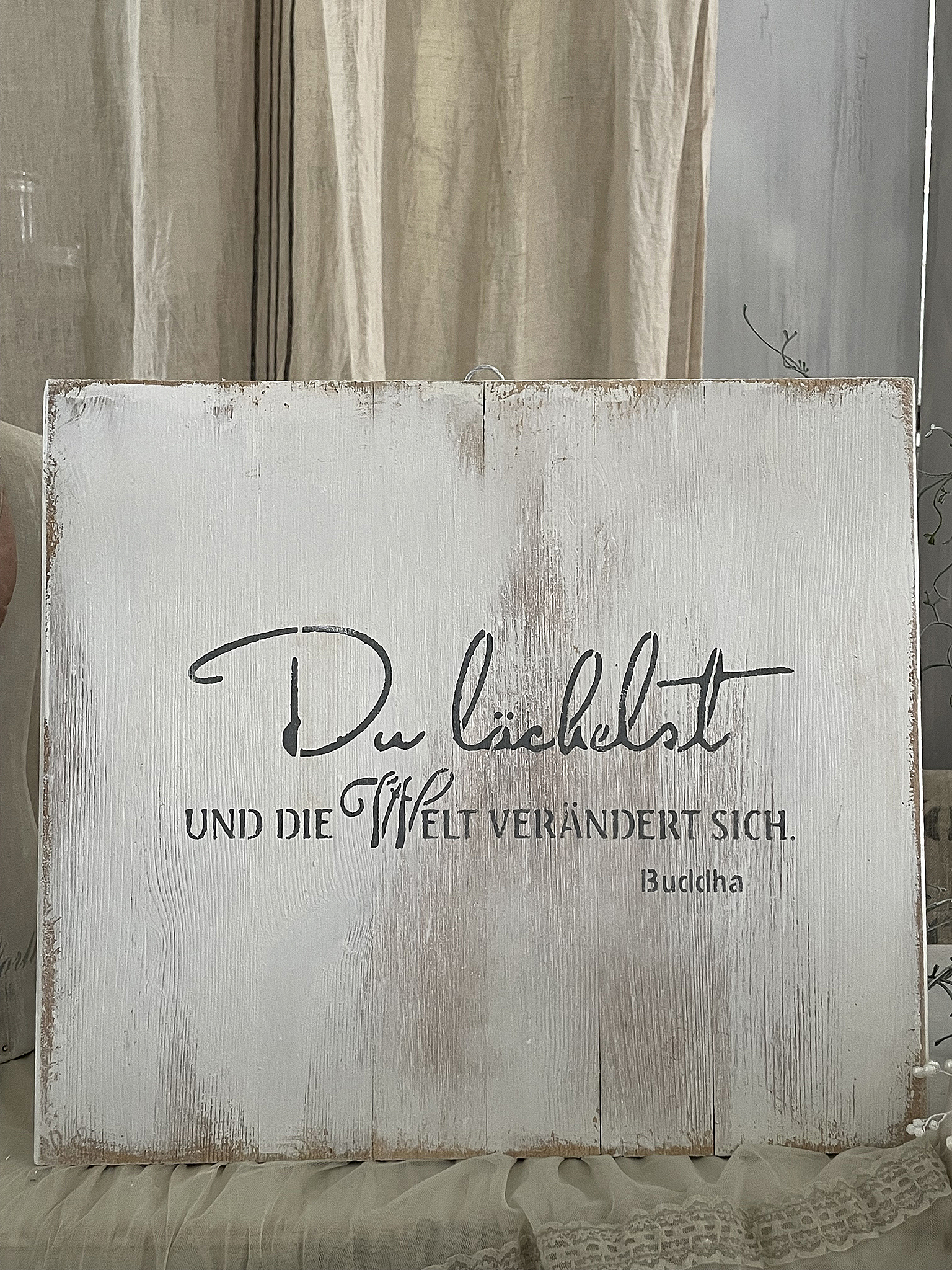 Holzschild mit einem inspirierenden Zitat von Buddha über das Lächeln und die Veränderung der Welt.