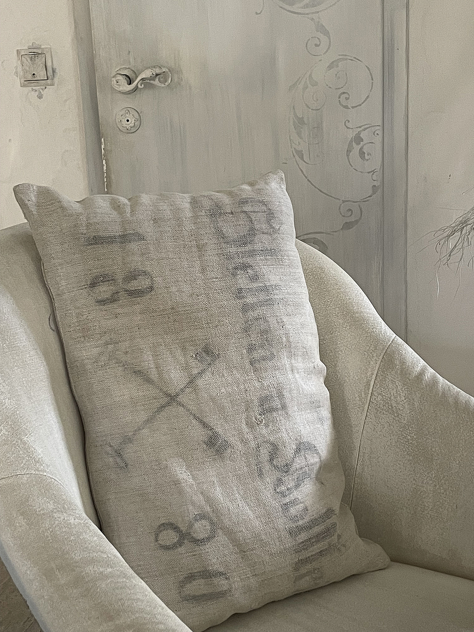 Dekoratives Kissen mit nostalgischem Design auf einem modernen Sessel Kissen mit vintage Schriftzügen und Motiven auf einem hellen Sessel
