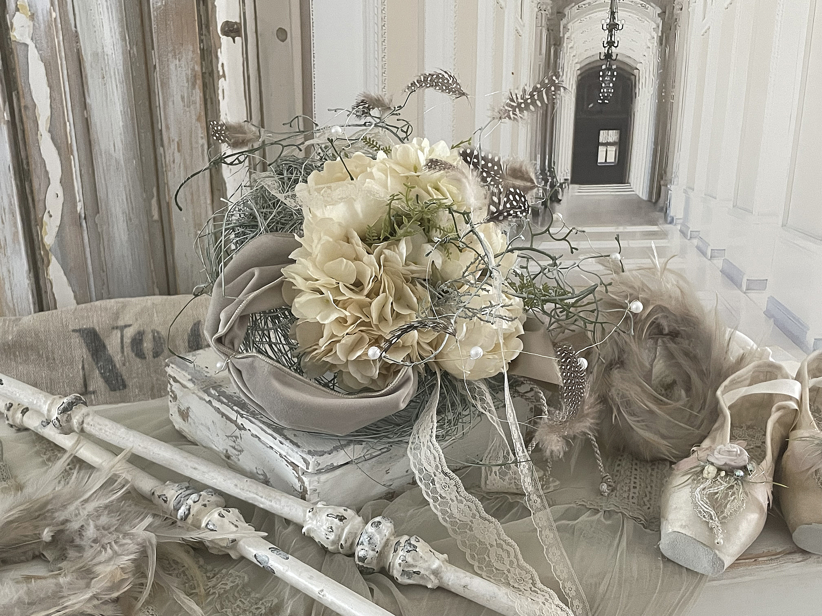 Eleganter Hochzeitsschmuck mit Blumenarrangement und Ballettschuhen Blumiger Dekorationsarrangement in neutralen Farbtönen mit Ballettschuhen und Federn auf einem Tisch