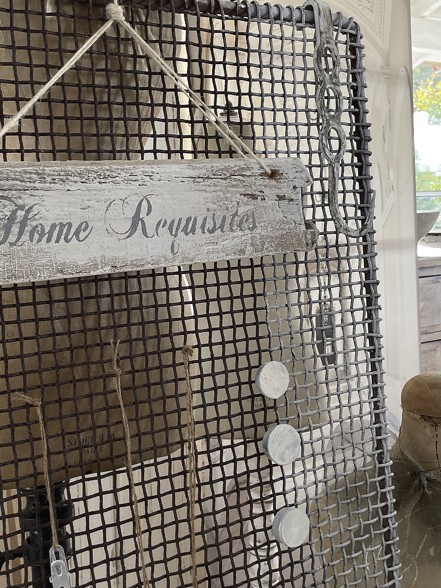 Dekoratives Schild mit der Aufschrift 'Home Requisites' und antiken Gegenständen Schild mit der Aufschrift 'Home Requisites', hängen an einem Drahtgitter mit verschiedenen dekorativen Elementen