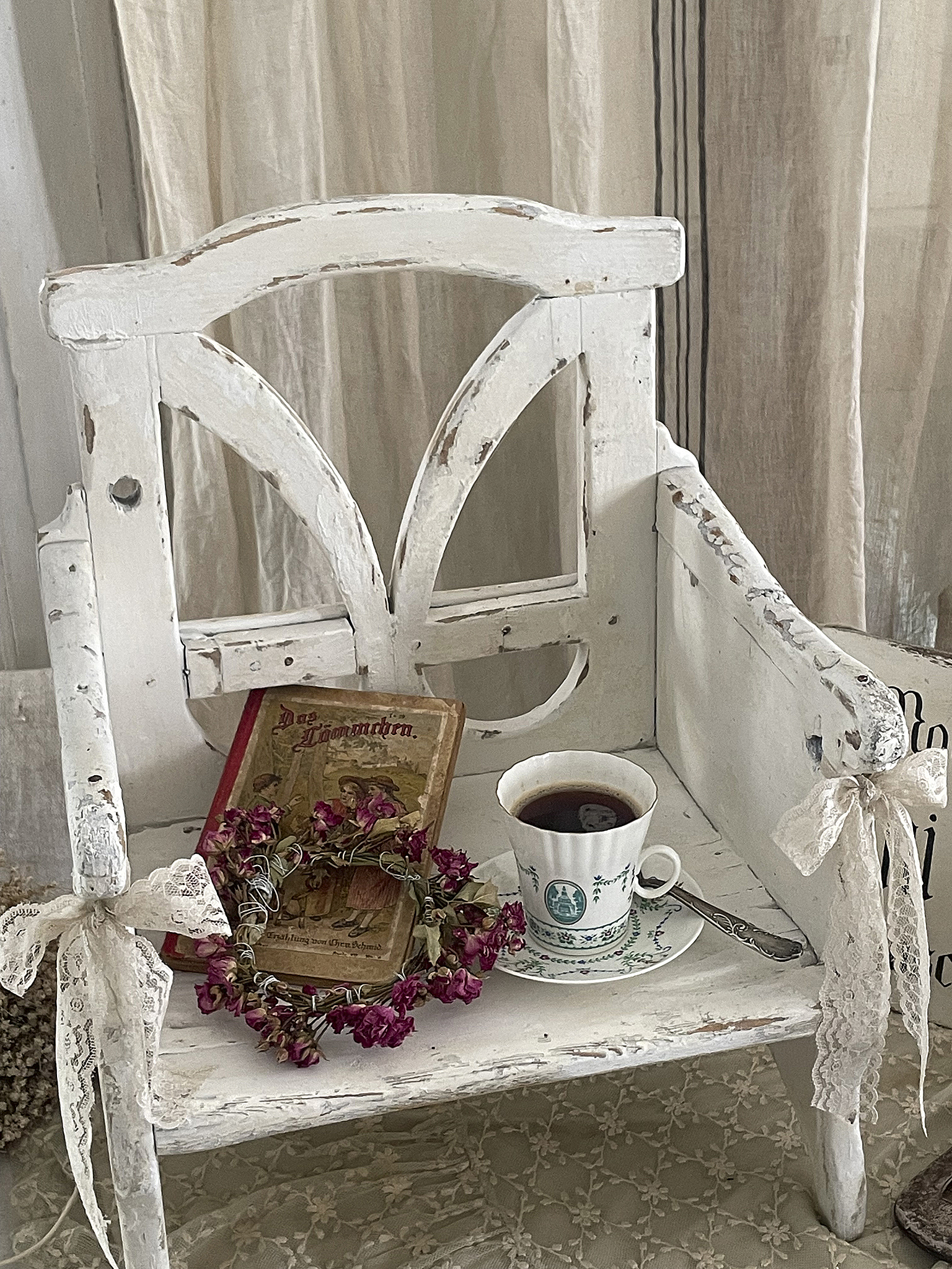 Vintage-Stuhl mit Kaffeetasse, einem alten Buch und einer Blumenkette auf einem Tisch