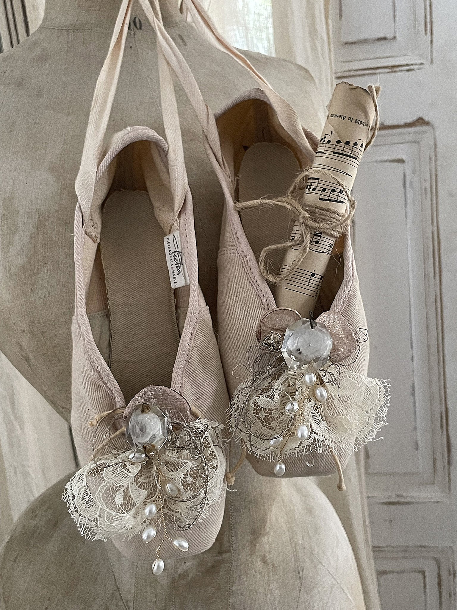 Elegante Ballettschuhe mit dekorativen Verzierungen und Notenblatt Schöne Ballettschuhe, kunstvoll verziert mit Spitze und Perlen, hängen an einer Schneiderpuppe.