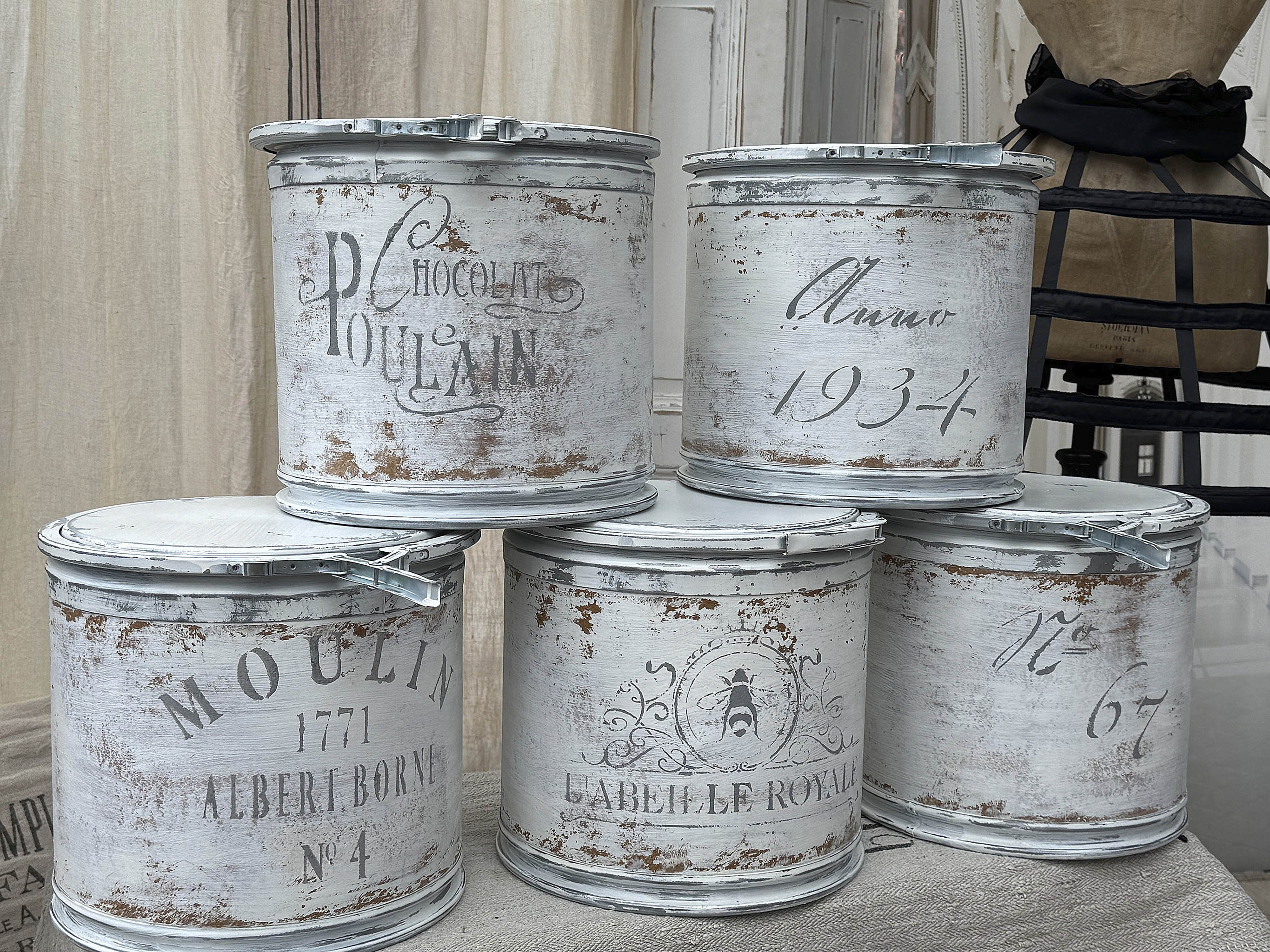 Historische Metallbehälter mit Beschriftungen für Chocolat Poulin und Moulin Fünf antike Metallbehälter mit nostalgischen Beschriftungen, die Chocolat Poulin und Moulin darstellen.