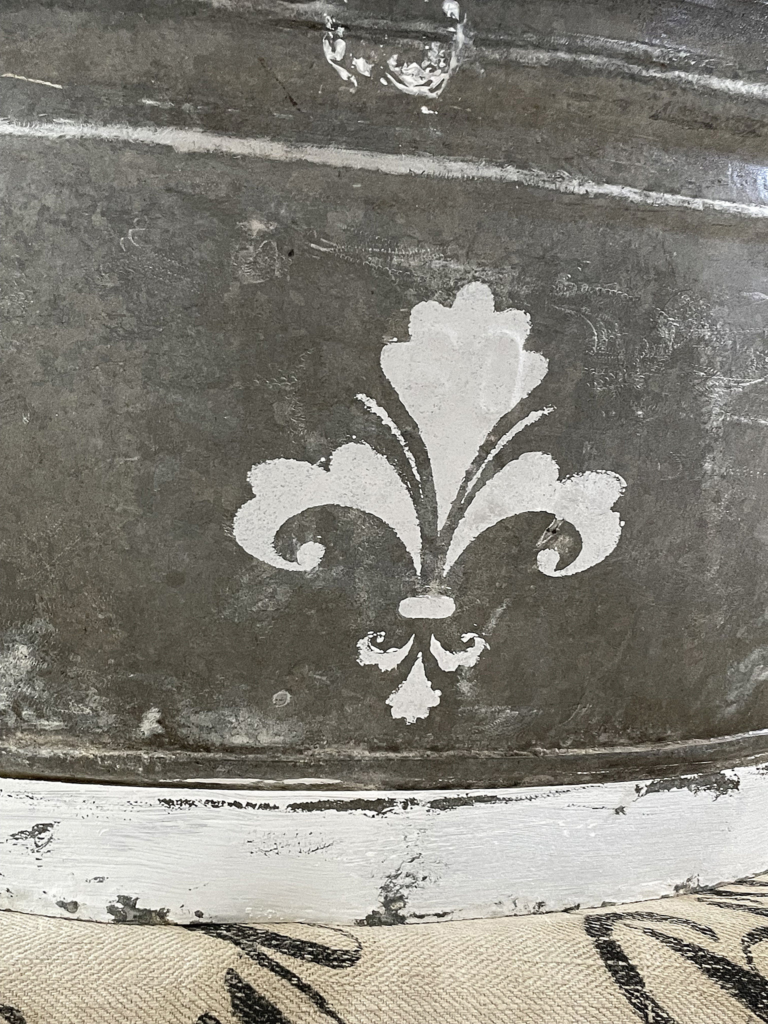 Zinkbehälter mit Fleur-de-Lis-Motiv Nahaufnahme eines Zinkbehälters mit einem weißen Fleur-de-Lis-Motiv auf grauer Oberfläche.
