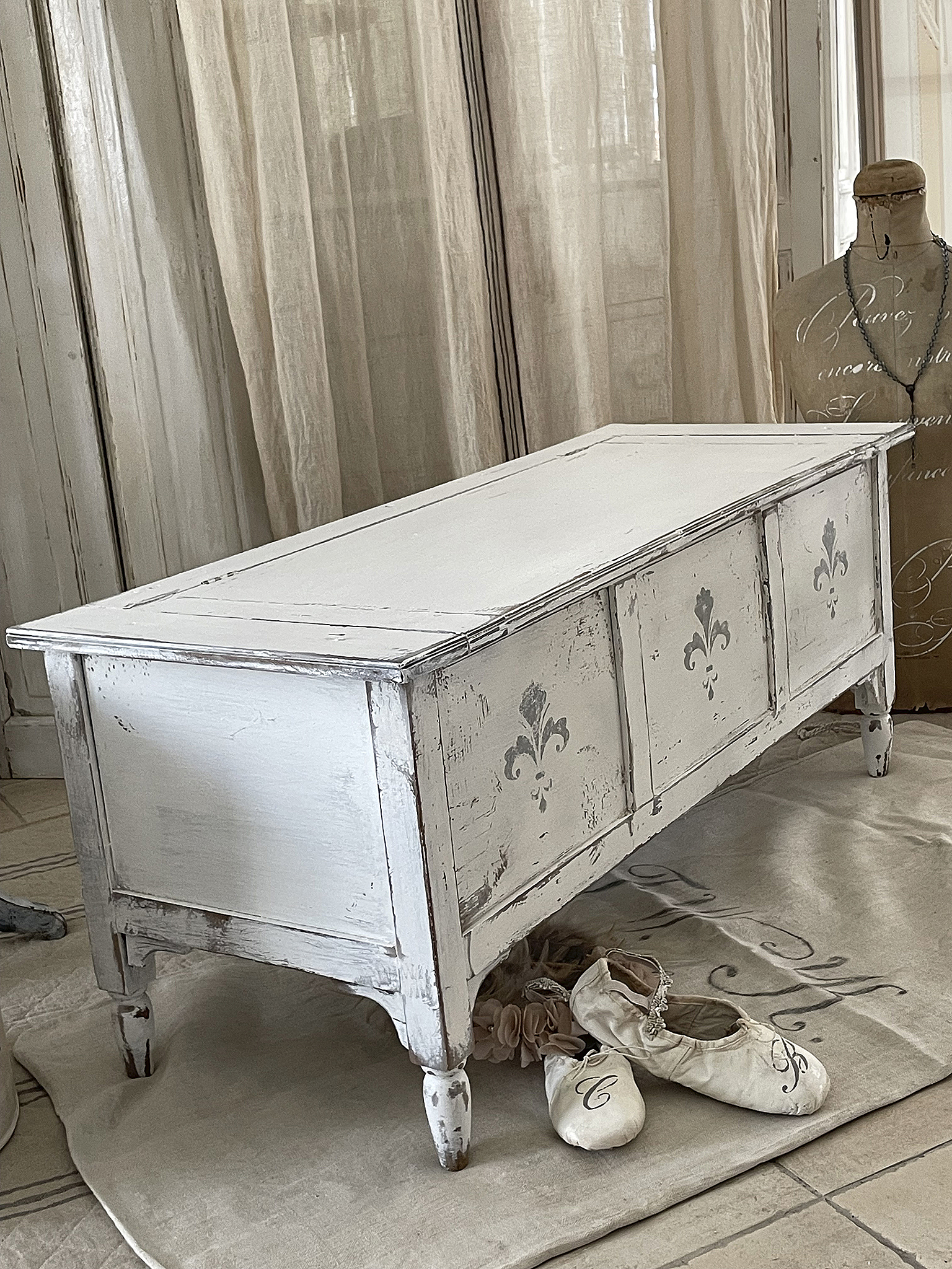 Antiker weißer Holzschrank mit detailverzierter Front Antiker weißer Holzschrank in einem stilvollen Raum, umgeben von Ballettschuhen und einem manniquin.