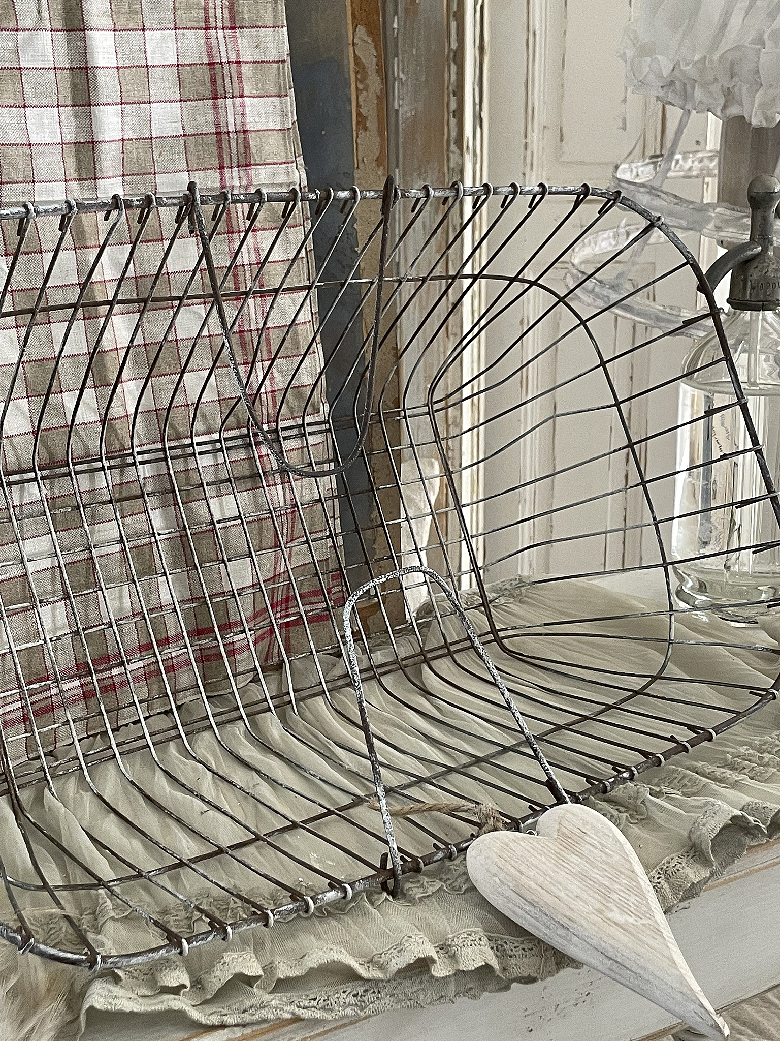 Dekorative Drahtkorb mit Herz, Landhausstil Drahtkorb auf einem Tisch mit einem Holzherz und einem gestreiften Tuch im Hintergrund