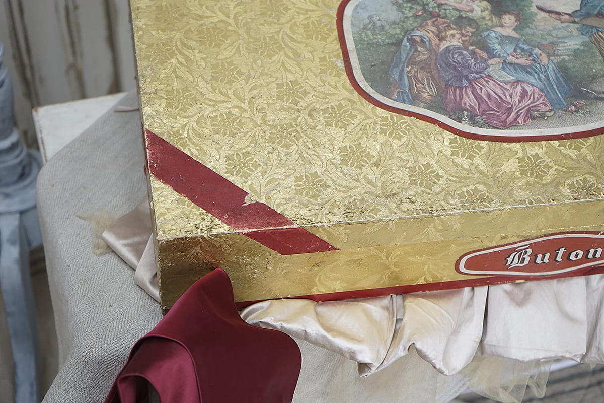 Detailansicht einer goldenen Geschenkbox mit rotem Band und buntem Motiv auf der Oberseite