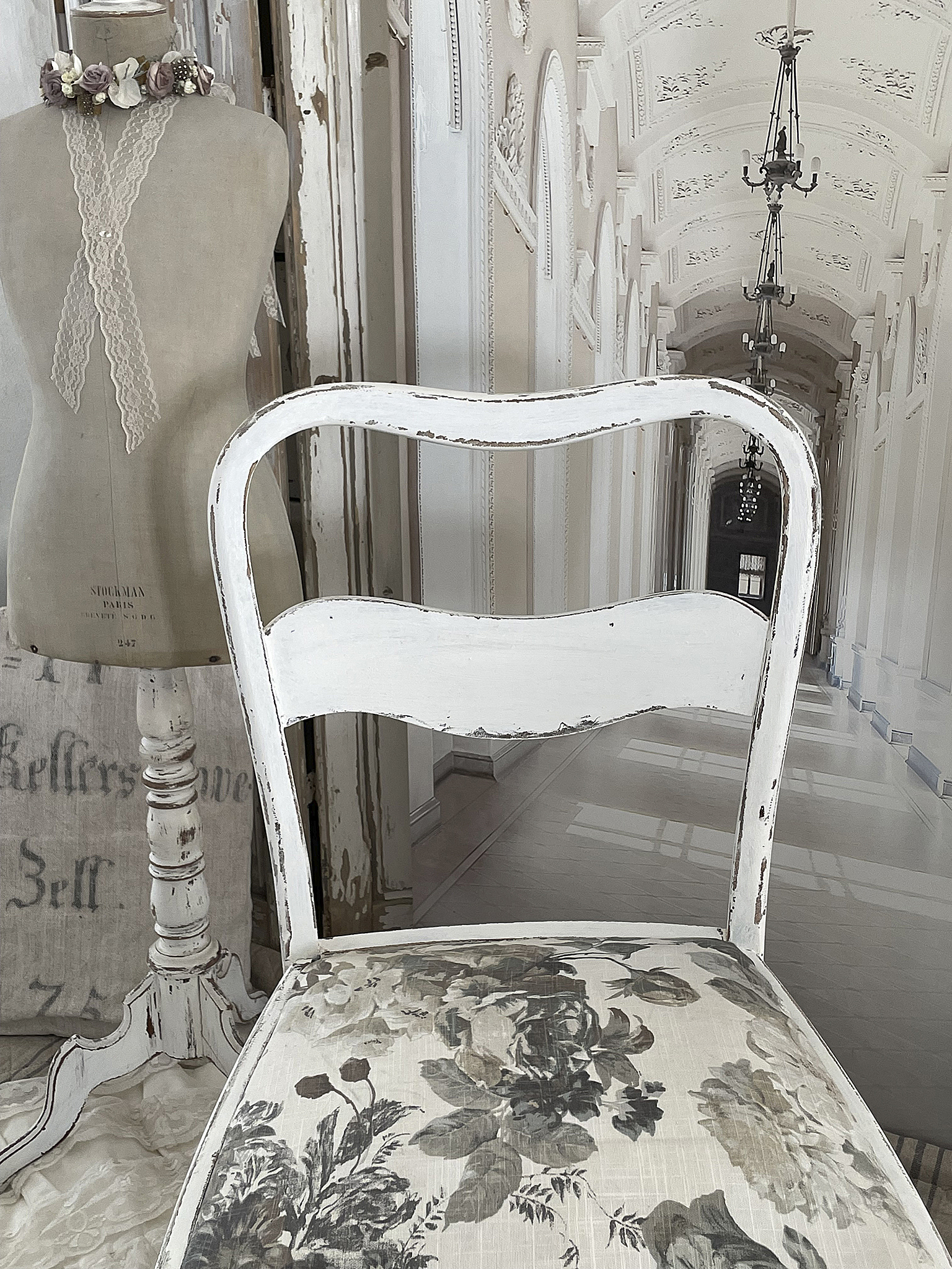 Rustikaler Stuhl mit floralem Design aus LInen Rückansicht eines weißen Stuhls mit floralem Stoffbezug und einer Schneiderpuppe im Hintergrund