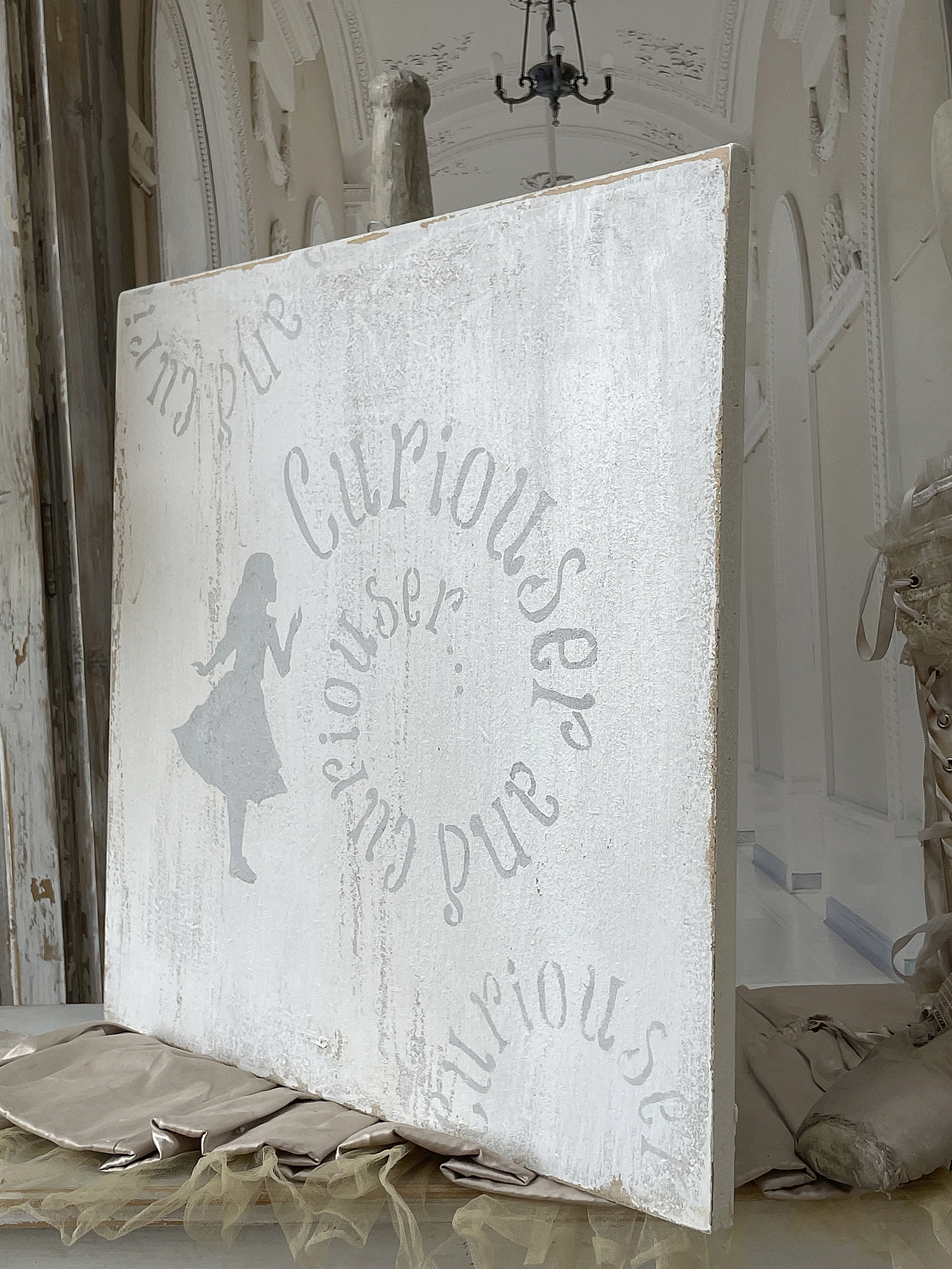 Dekorative Wandtafel mit dem Schriftzug 'Curiouser and Curious' Wandtafel im Vintage-Stil mit dem Aufdruck 'Curiouser and Curious' und einer stilisierten Figur eines Mädchens.