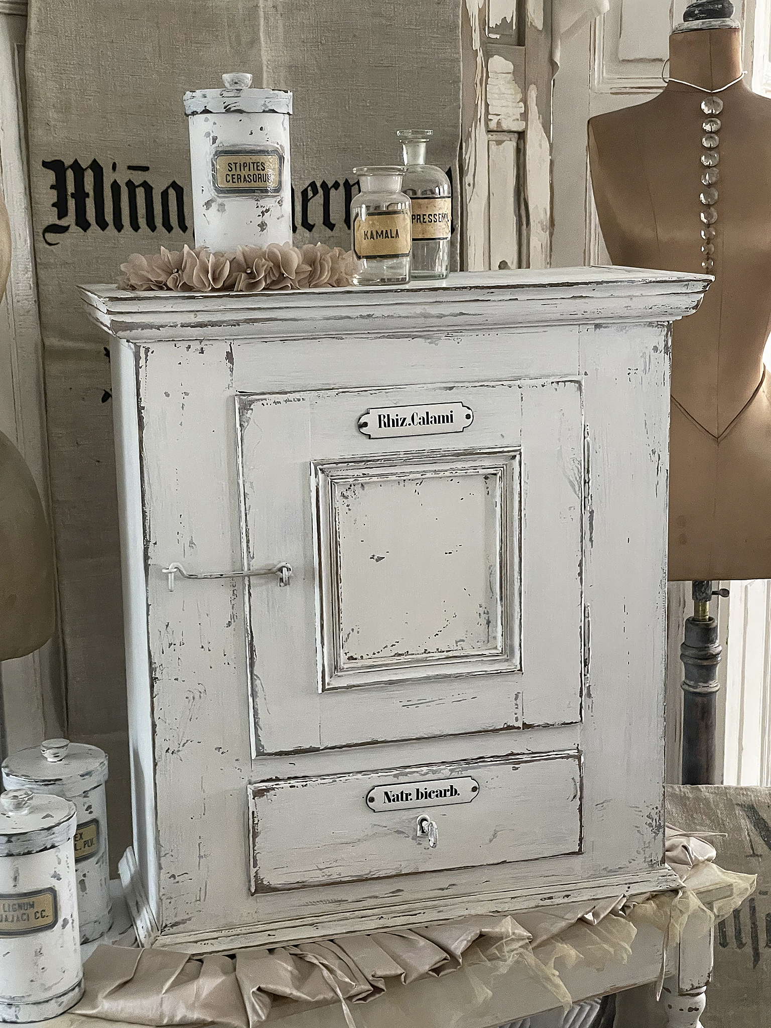 Vintage Kommode mit Retro-Glasgefäßen und Schubladen Eine antike weiße Kommode mit dekorativen Glasgefäßen und Etiketten auf den Schubladen.