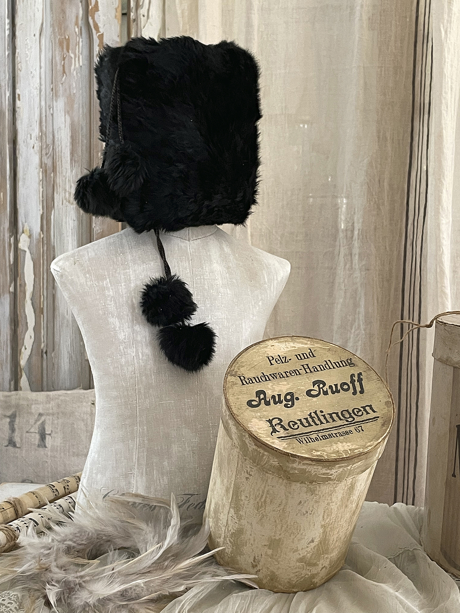 Schwarze Pelzmütze auf einer Schaufensterpuppe mit historischem Karton Schwarze Pelzmütze auf einer Schaufensterpuppe, daneben ein historischer Karton mit der Aufschrift 'Pelz- und Rauwaren-Handlung Aug. Ruoff Reutlingen'
