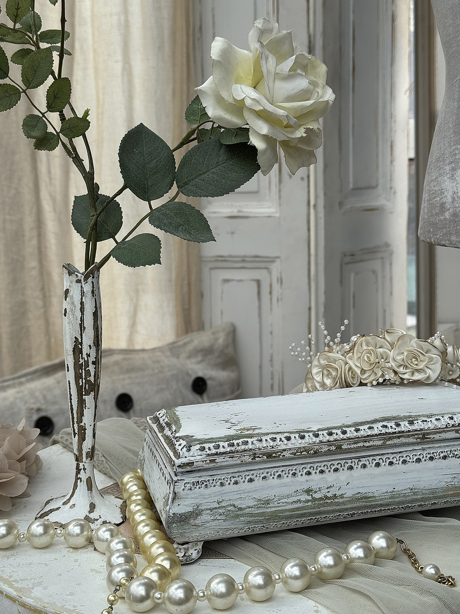 Dekorativer Tisch mit blassgelber Rose und Schmuckkästchen Schöner Tisch mit einer blassgelben Rose in einer Vase, einem eleganten Schmuckkästchen und Perlenkette.