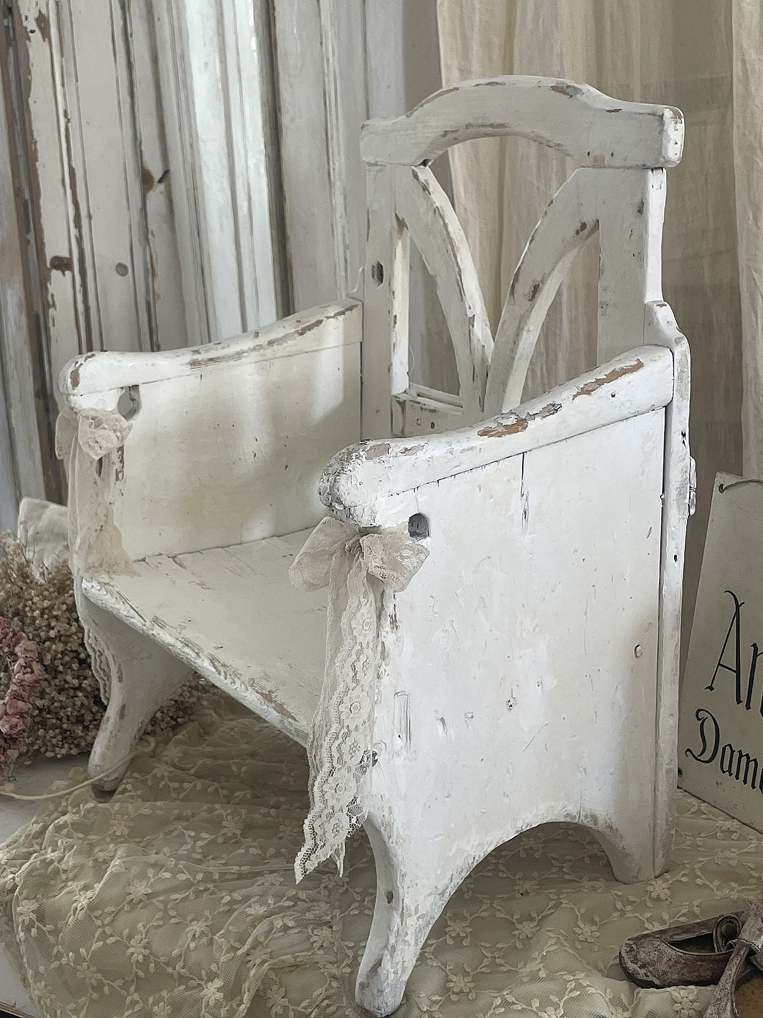 Antiker Holzstuhl, weiß gestrichen, mit dekorativer Spitze und patinierten Details.