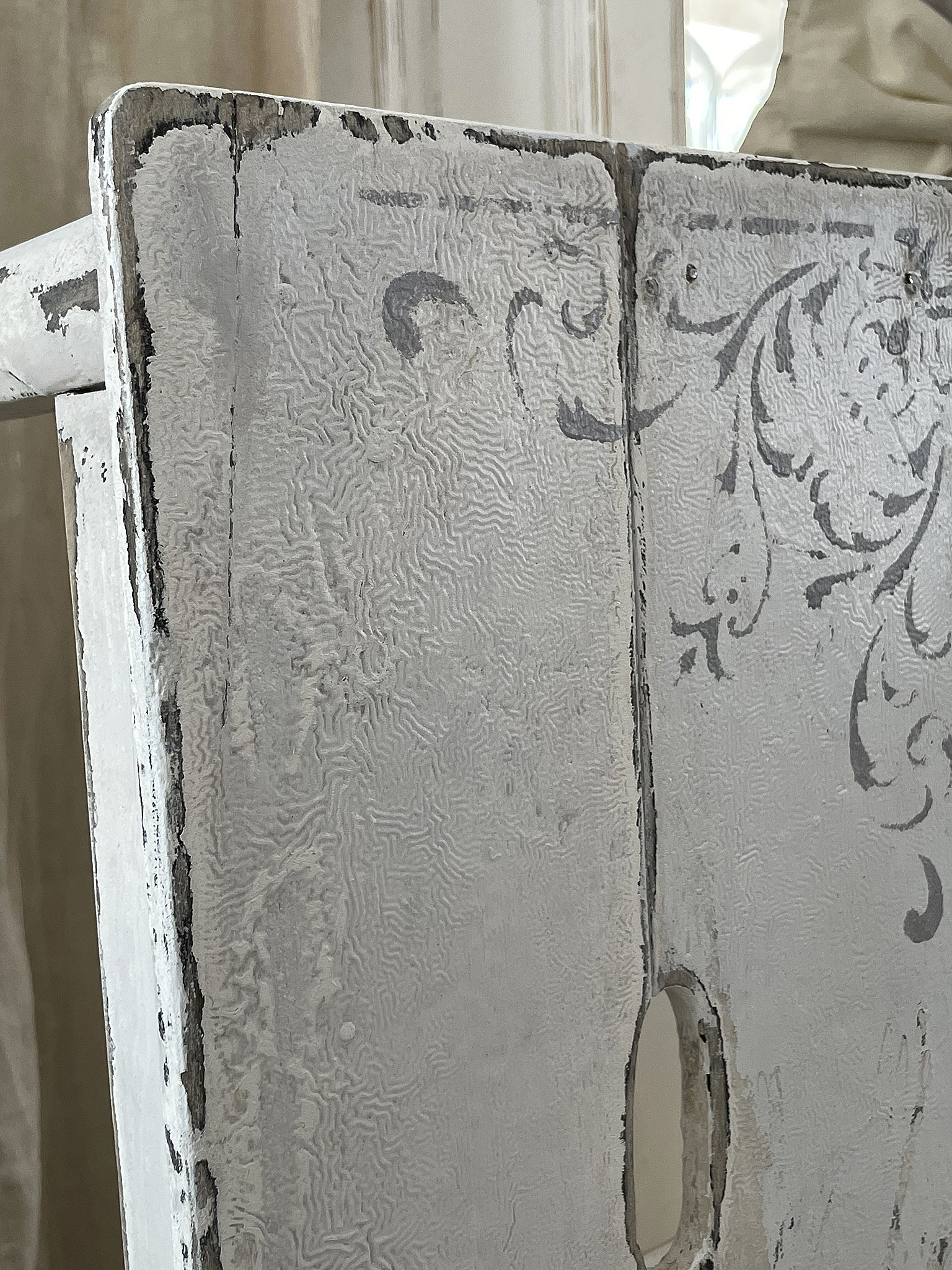 Detailansicht eines antiken, dekorativ bemalten Holzmöbels in Weiß Nahaufnahme eines dekorativen, weißen Holzmöbels mit feiner Struktur und floralem Muster.
