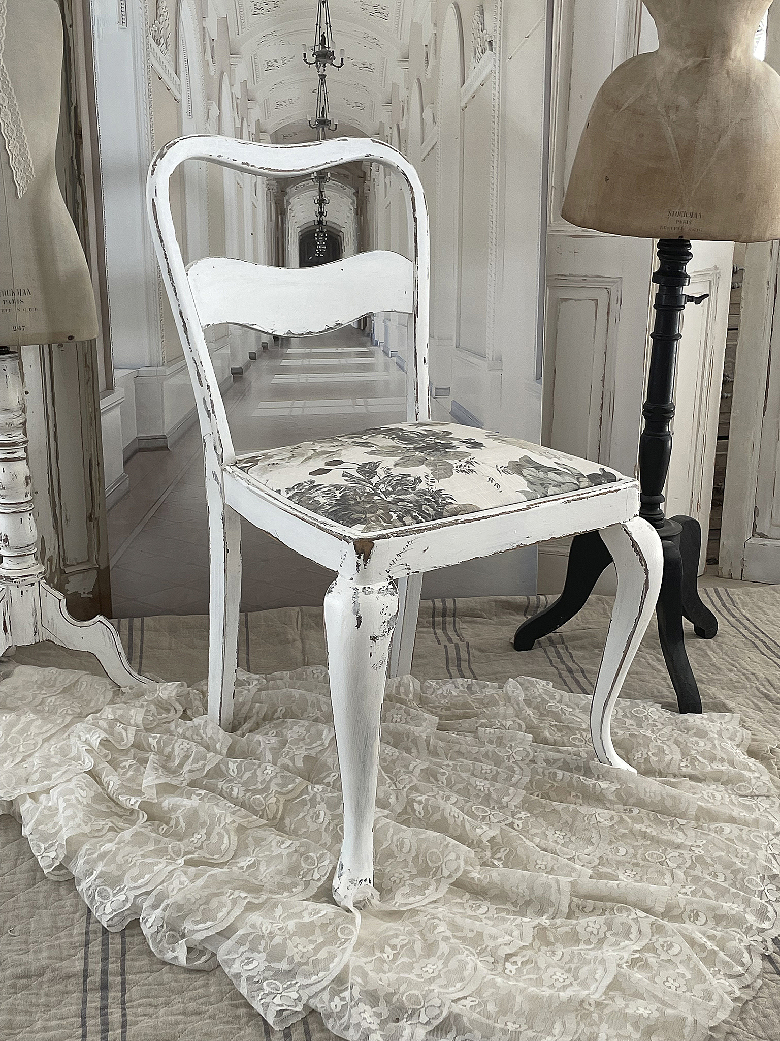 Vintage Stuhl mit floraler Polsterung im eleganten Ambiente Weißer Vintage-Stuhl mit floralem Sitz, umgeben von einem eleganten Raum mit dekorativem Stoff.