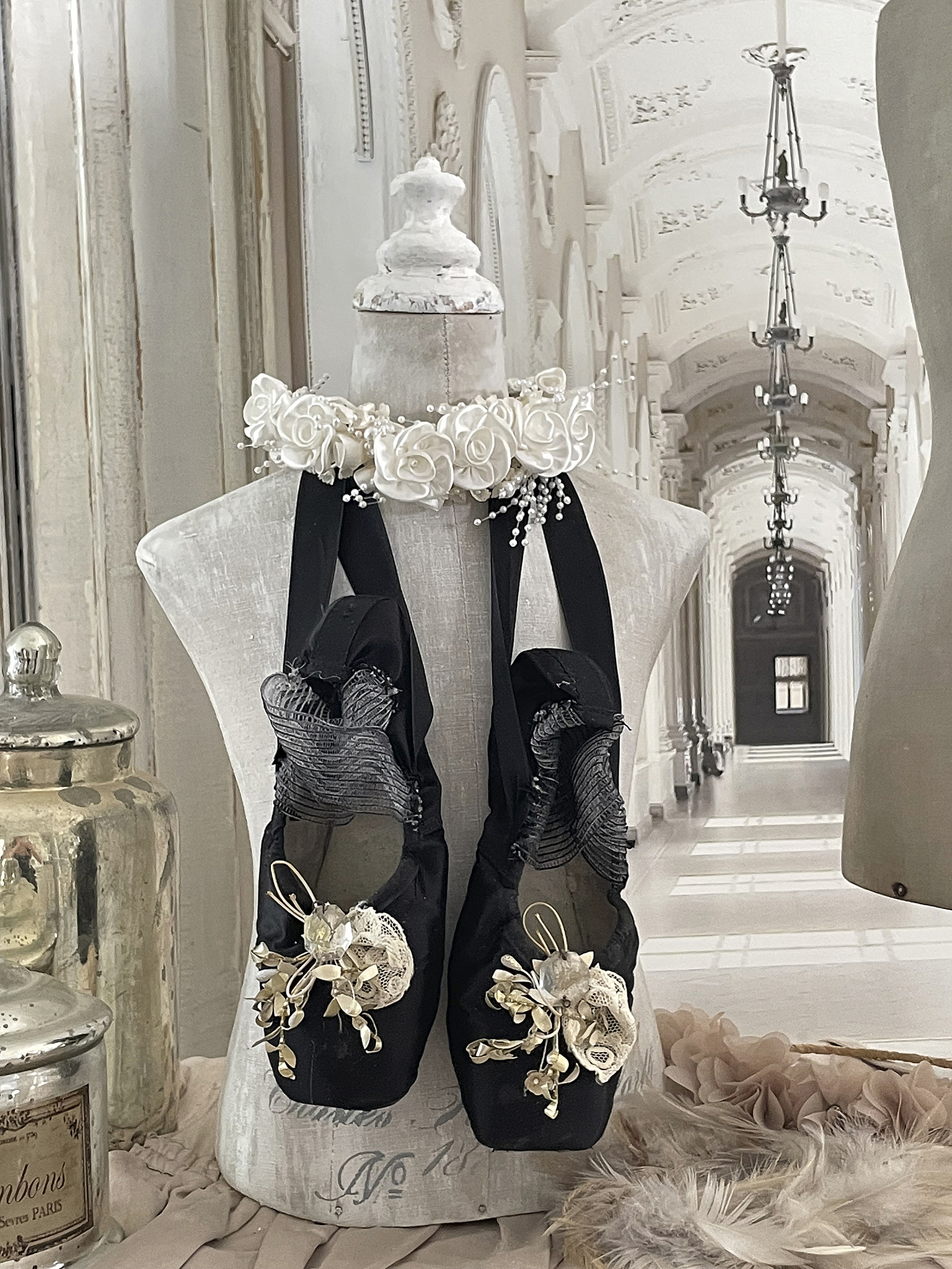 Elegante Ballettschuhe mit floralen Akzenten auf einer Schneiderpuppe Schneiderpuppe mit dekorativen schwarzen Ballettschuhen und einer blumigen Halskette in einem hellen Raum