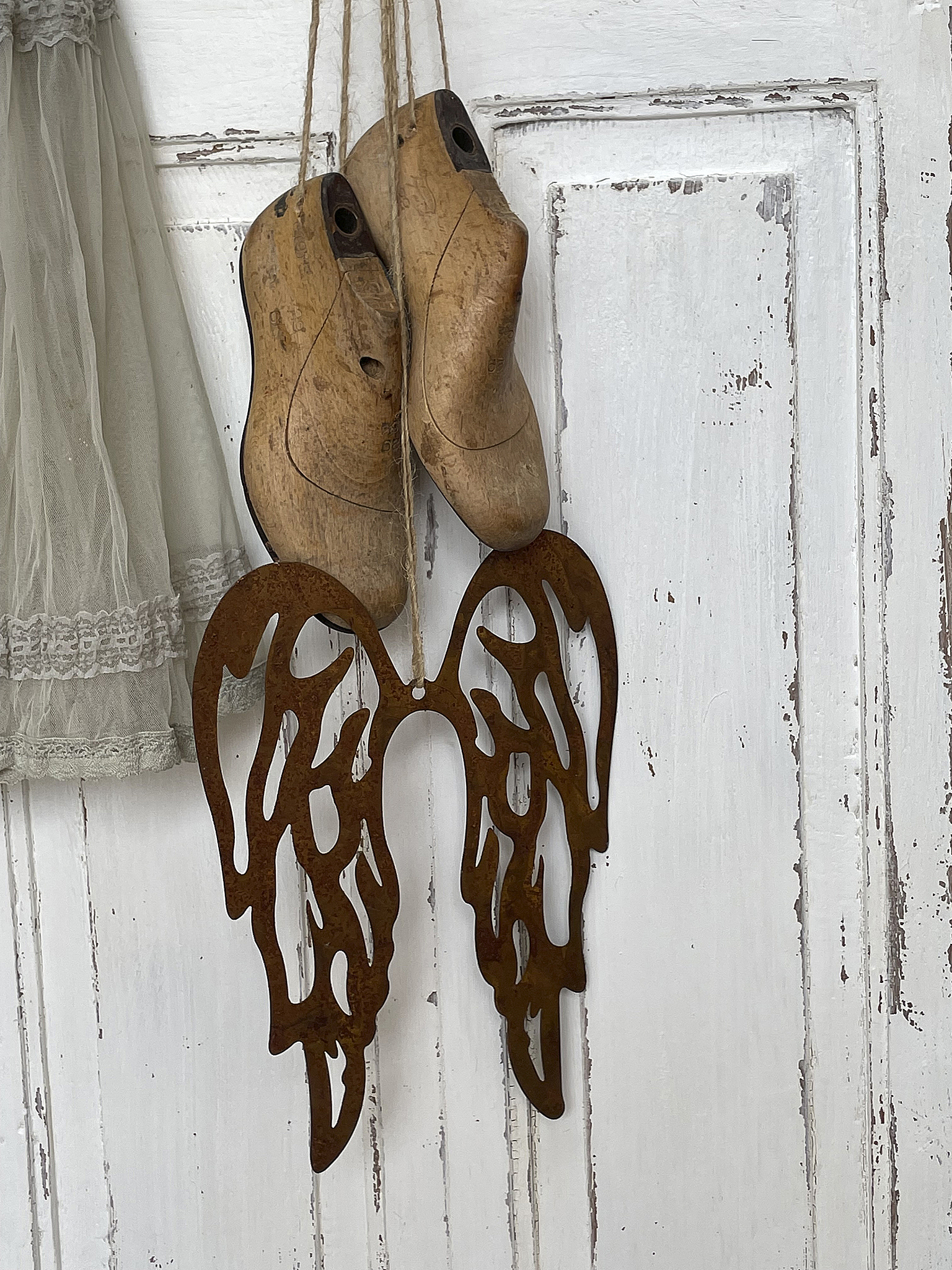 Zwei Holzschuhe und eine metallene Flügel-Dekoration an einer weißen Wand