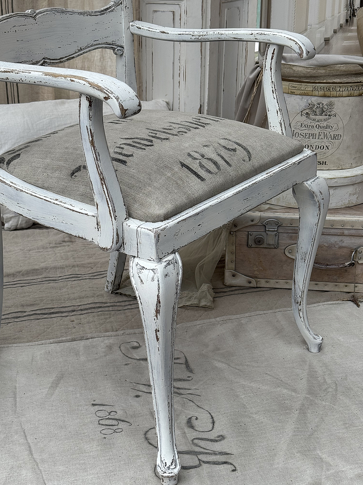 Vintage weißer Stuhl mit grauem Bezug und Patina Detailansicht eines weißen Vintage-Stuhls mit grauem Sitzpolster und verziertem Design