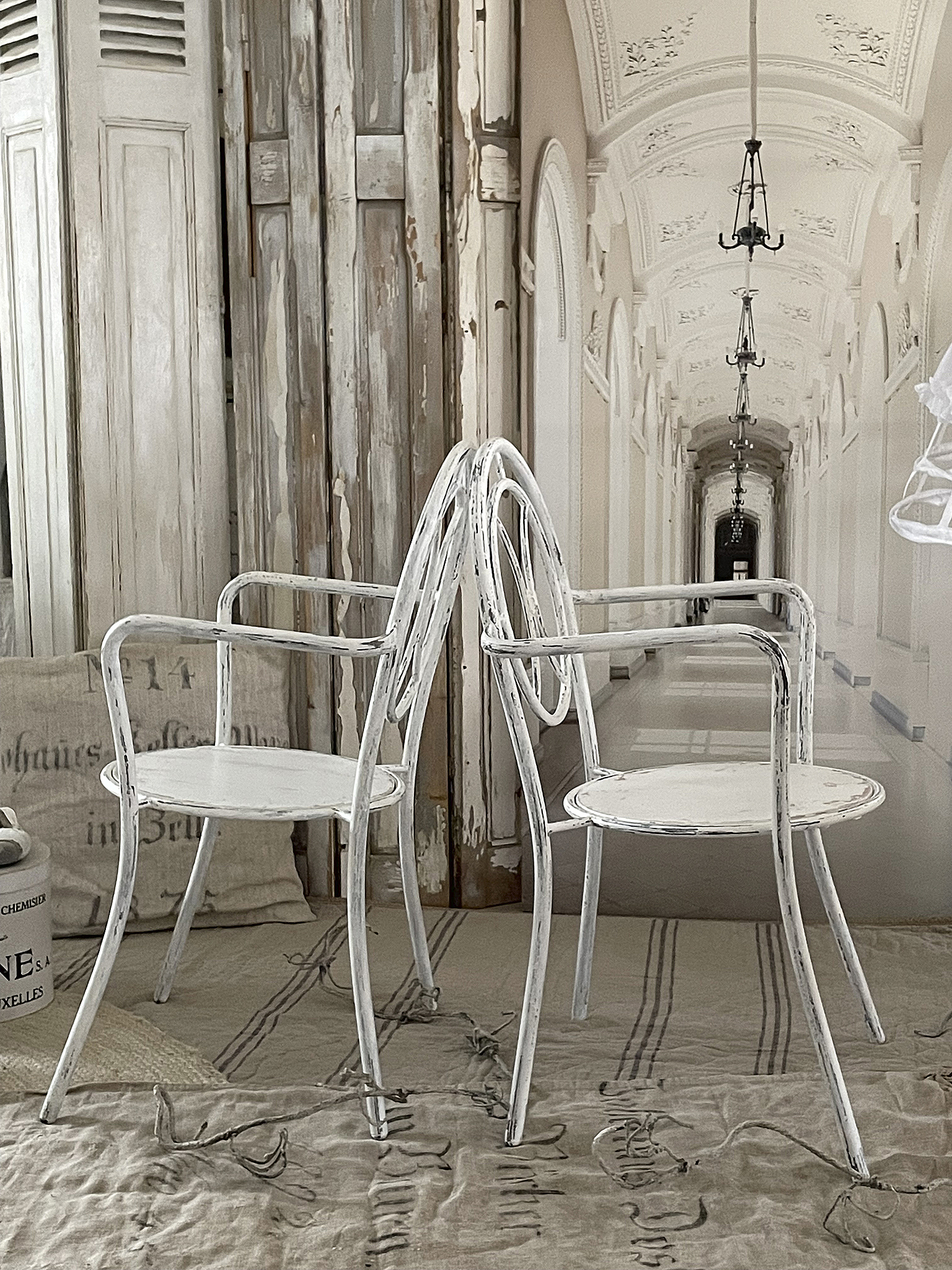 Zwei weiße Stühle im vintage Stil vor einem hellen Hintergrund Zwei weiße Vintage-Stühle, die Rücken an Rücken stehen, auf einem beige Teppich in einem elegant eingerichteten Raum.