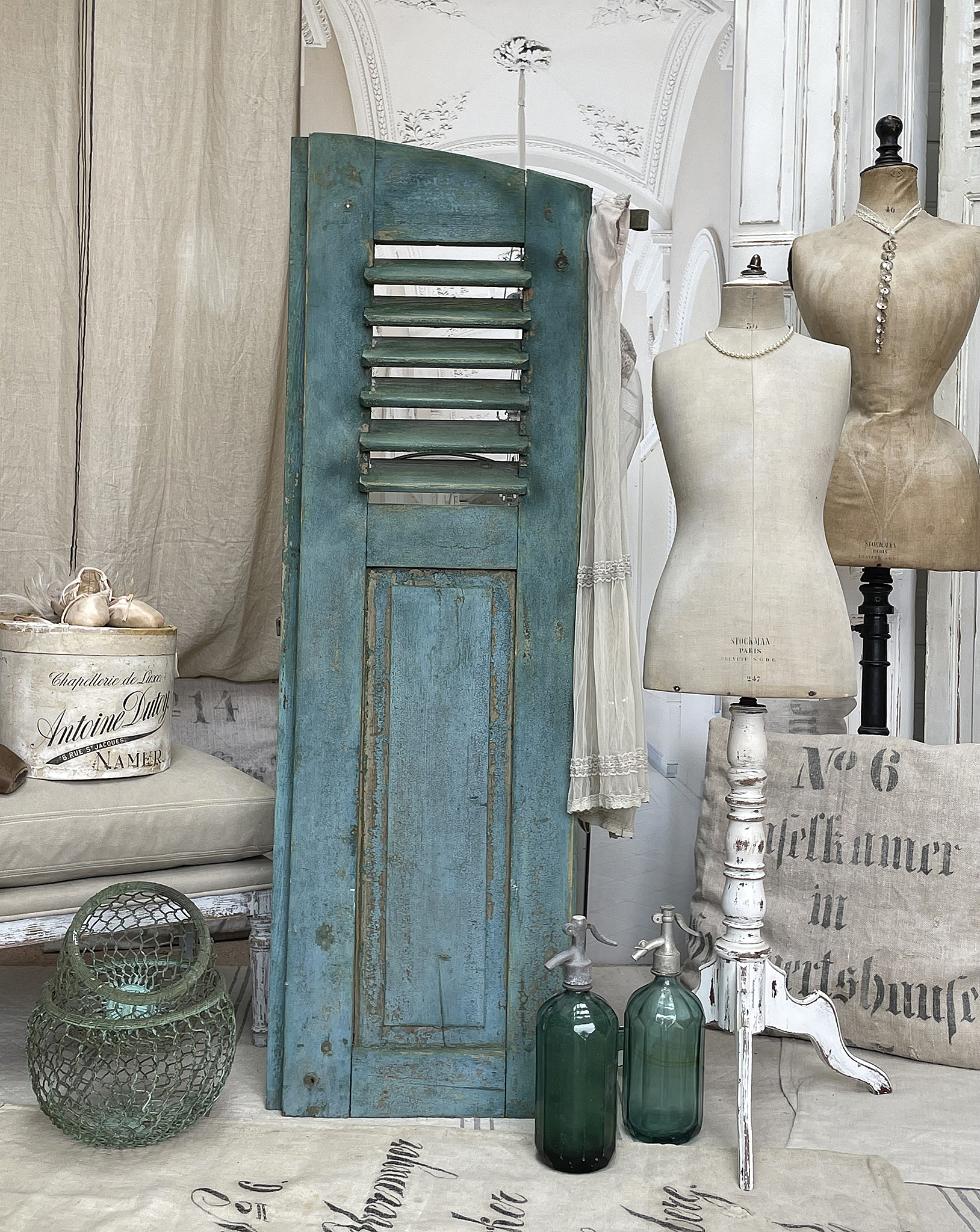 Stilvolles Vintage-Dekor mit blauem Holzschrank und Glasflaschen Dekoratives Arrangement mit blauem Holzschrank, zwei grünen Glasflaschen und Schneiderpuppen
