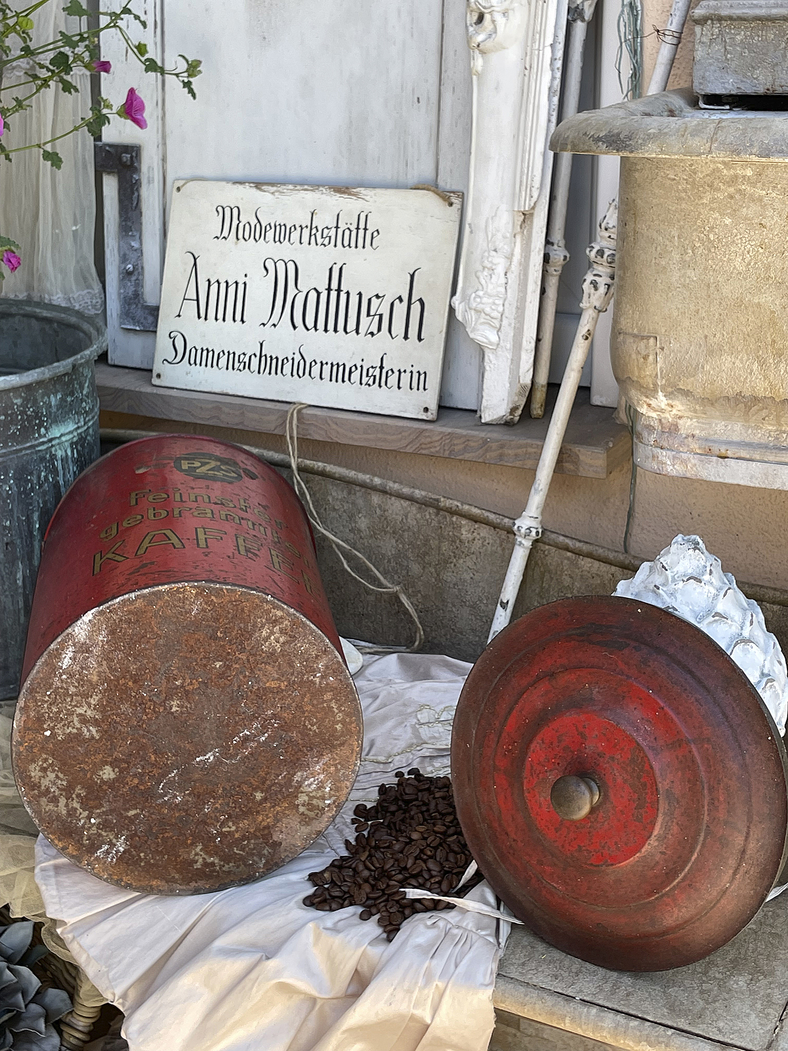 Antike Kaffeekanne und dekorative Elemente vor der Schneiderwerkstatt Rote Kaffeekanne und Kaffeebohnen vor der Modewerkstätte Anni Mattusch