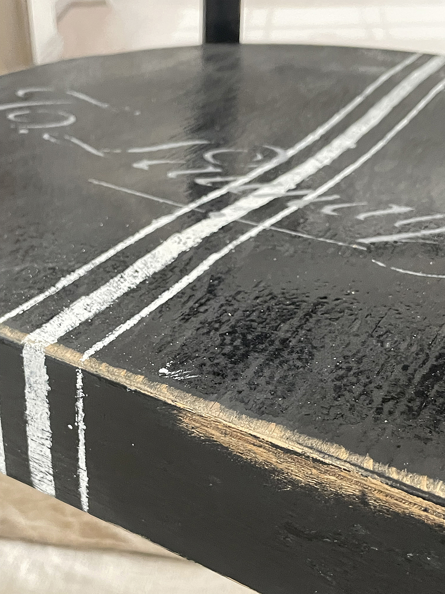 Detailaufnahme eines schwarzen Tischs mit weißen Linien und rustikalem Finish Nahaufnahme eines schwarzen Tisches mit weißen Streifen und sichtbarem Holzfinish
