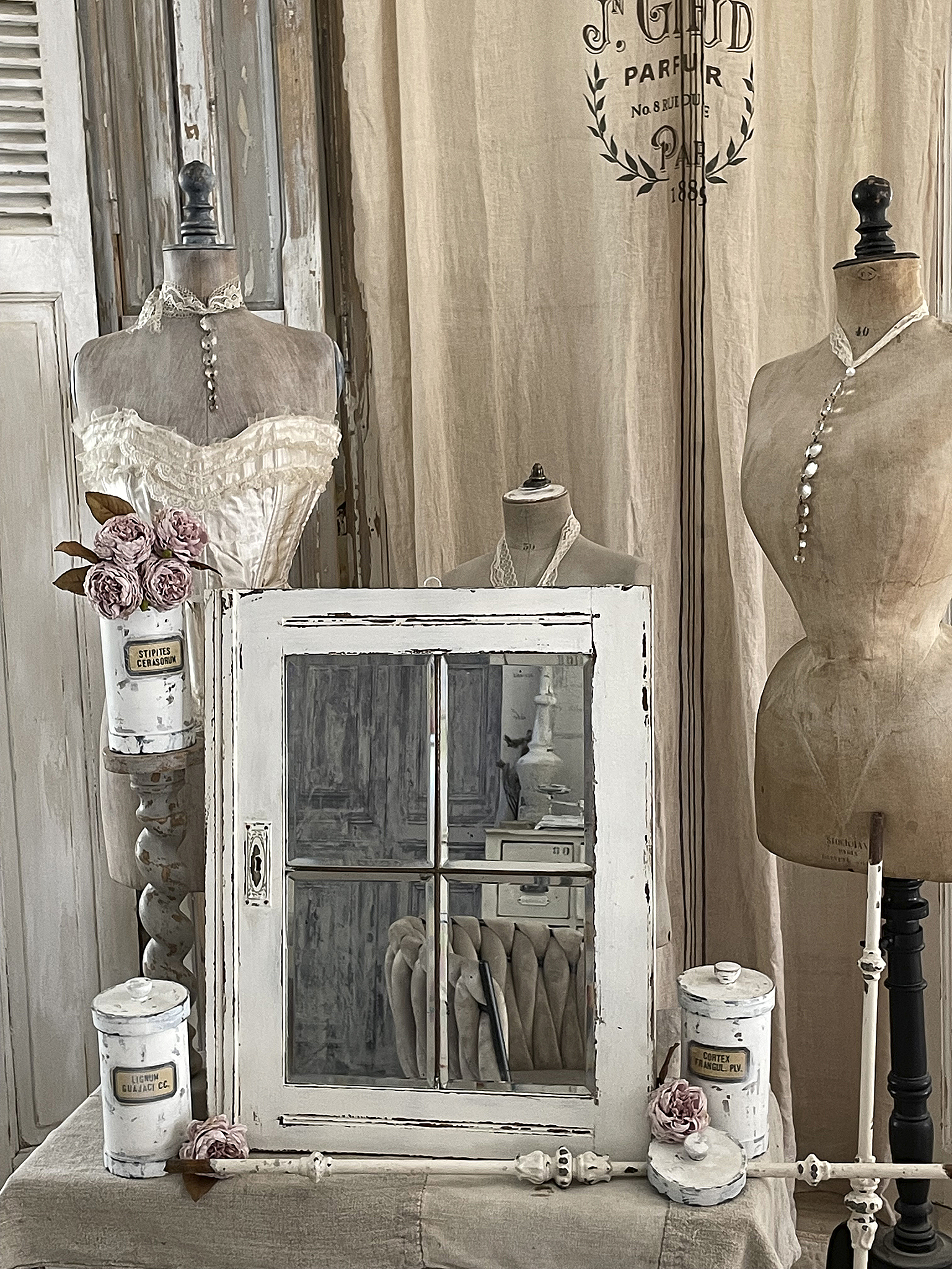 Vintage Dekoration mit Spiegel und Mannequins Ein stilvolles Arrangement mit einem weißen Spiegel, zwei Mannequins, einem Blütenarrangement und dekorativen Objekten.