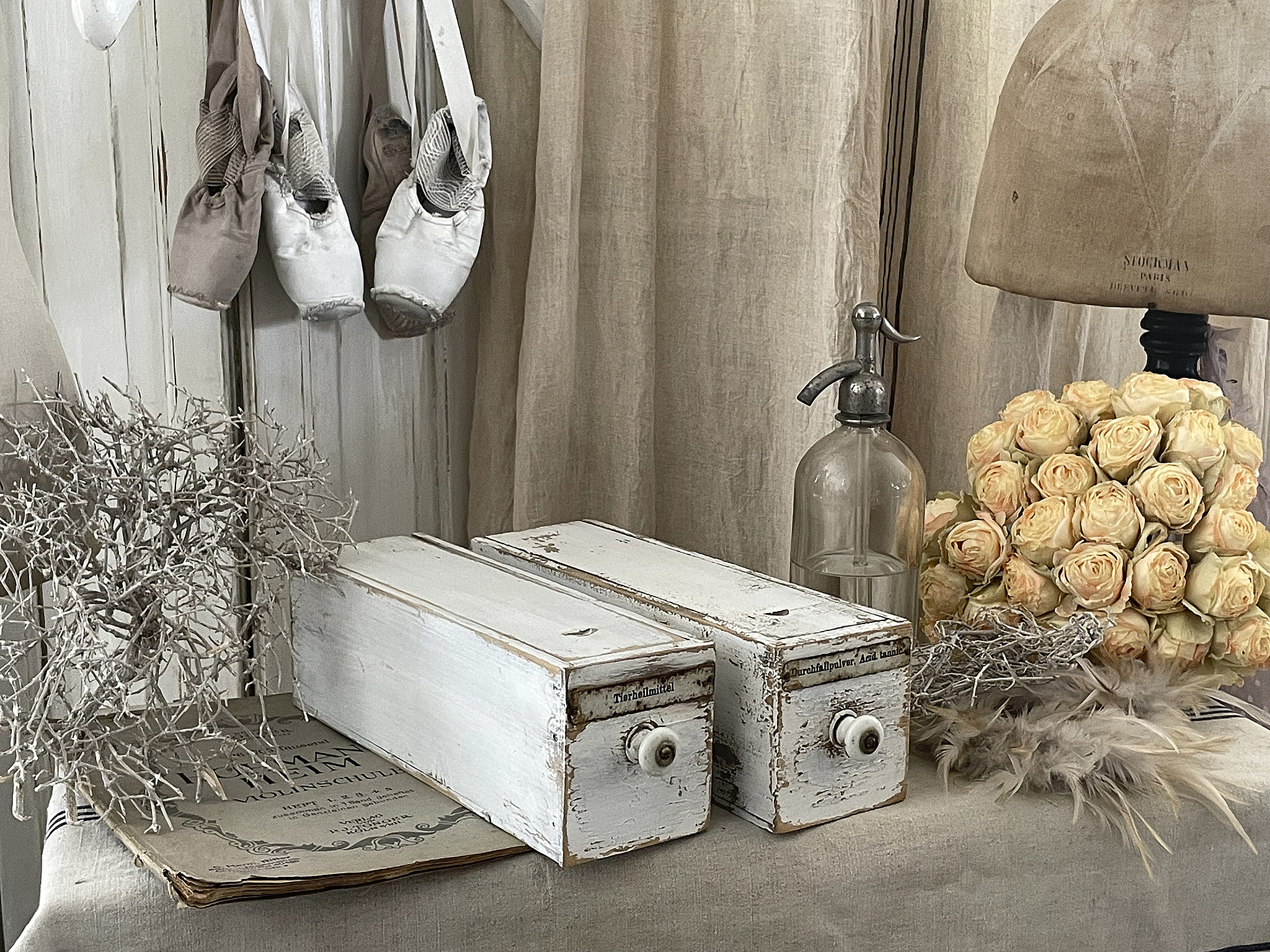 Stillleben mit weißen Schubladen, Ballettschuhen, einer alten Sprühflasche und Trockenblumen