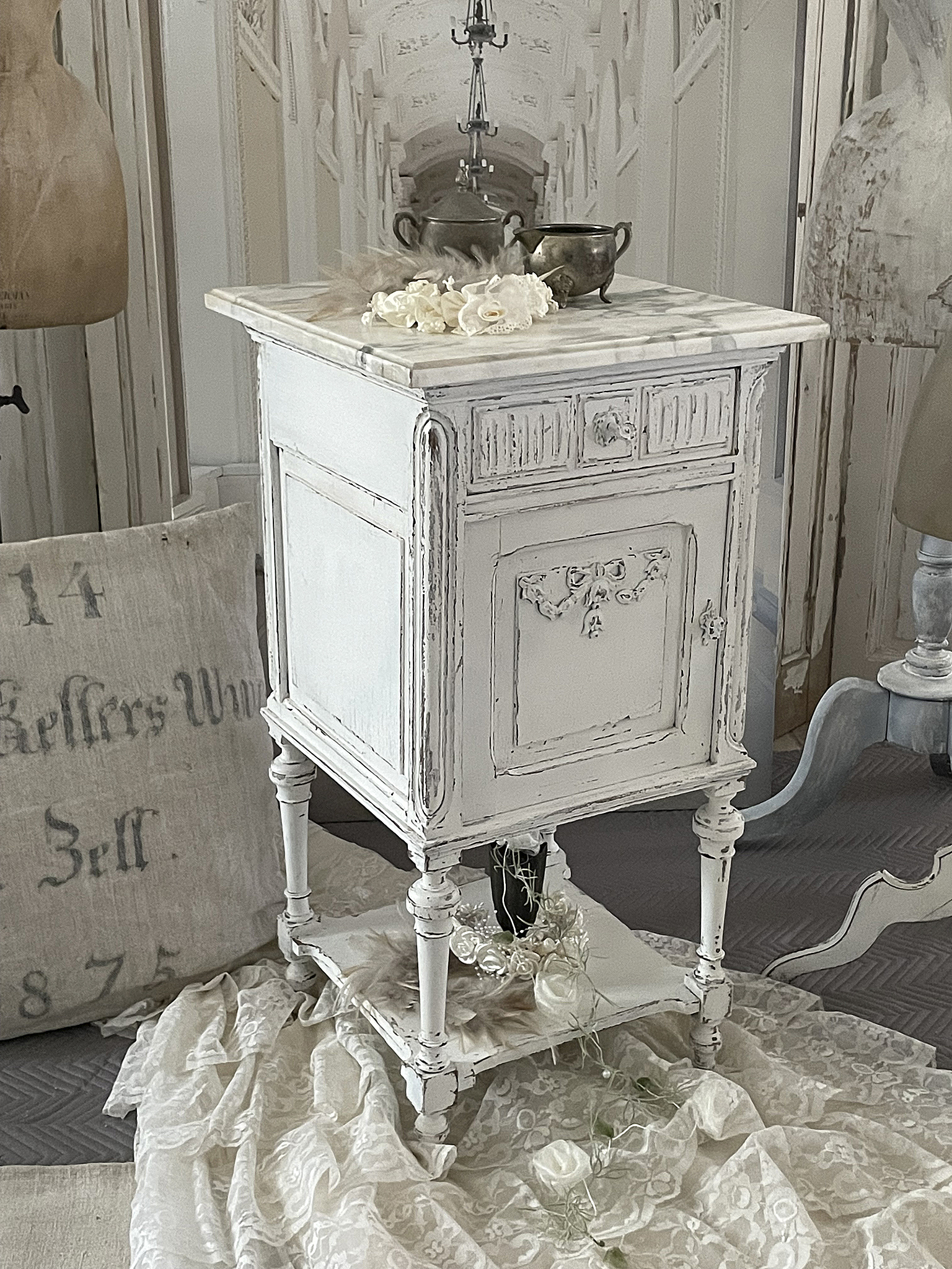 Eleganter vintage Beistelltisch mit weißer Patina und dekorativem Marmoraufsatz Vintagestil Beistelltisch mit marbiriertem Top und floraler Dekoration auf dem Tisch