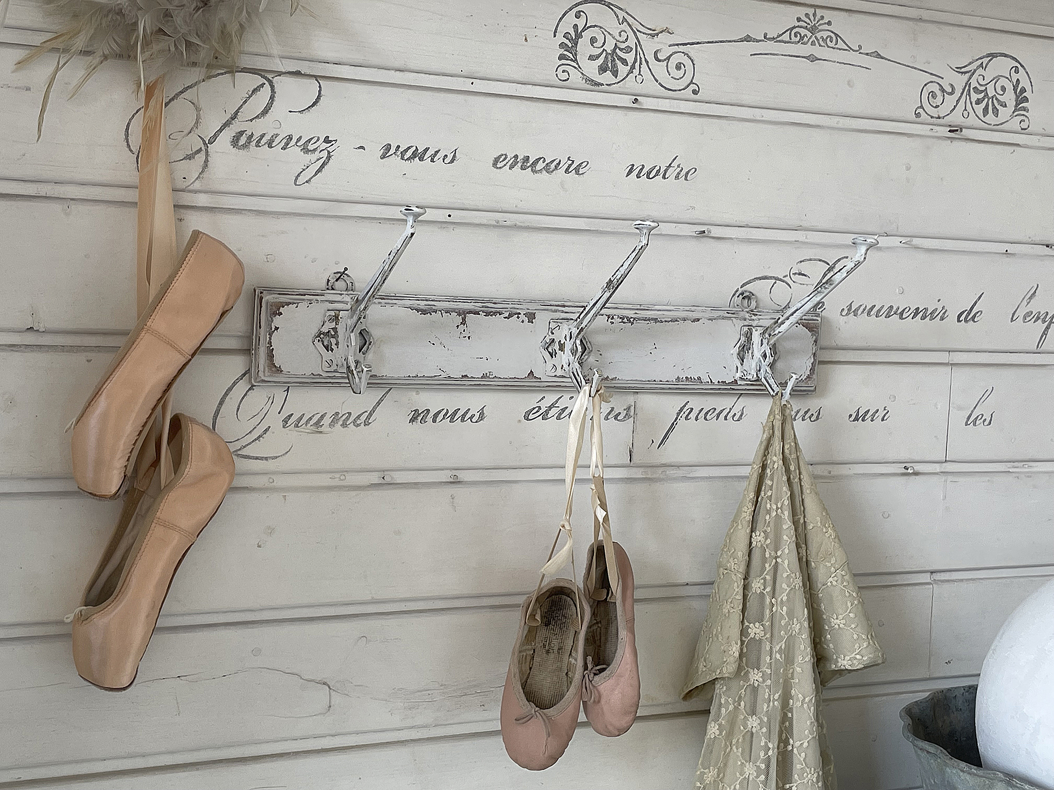 Ballettschuhe und ein Kleid hängen an einem rustikalen Hakenbrett vor einer dekorativen Wand.