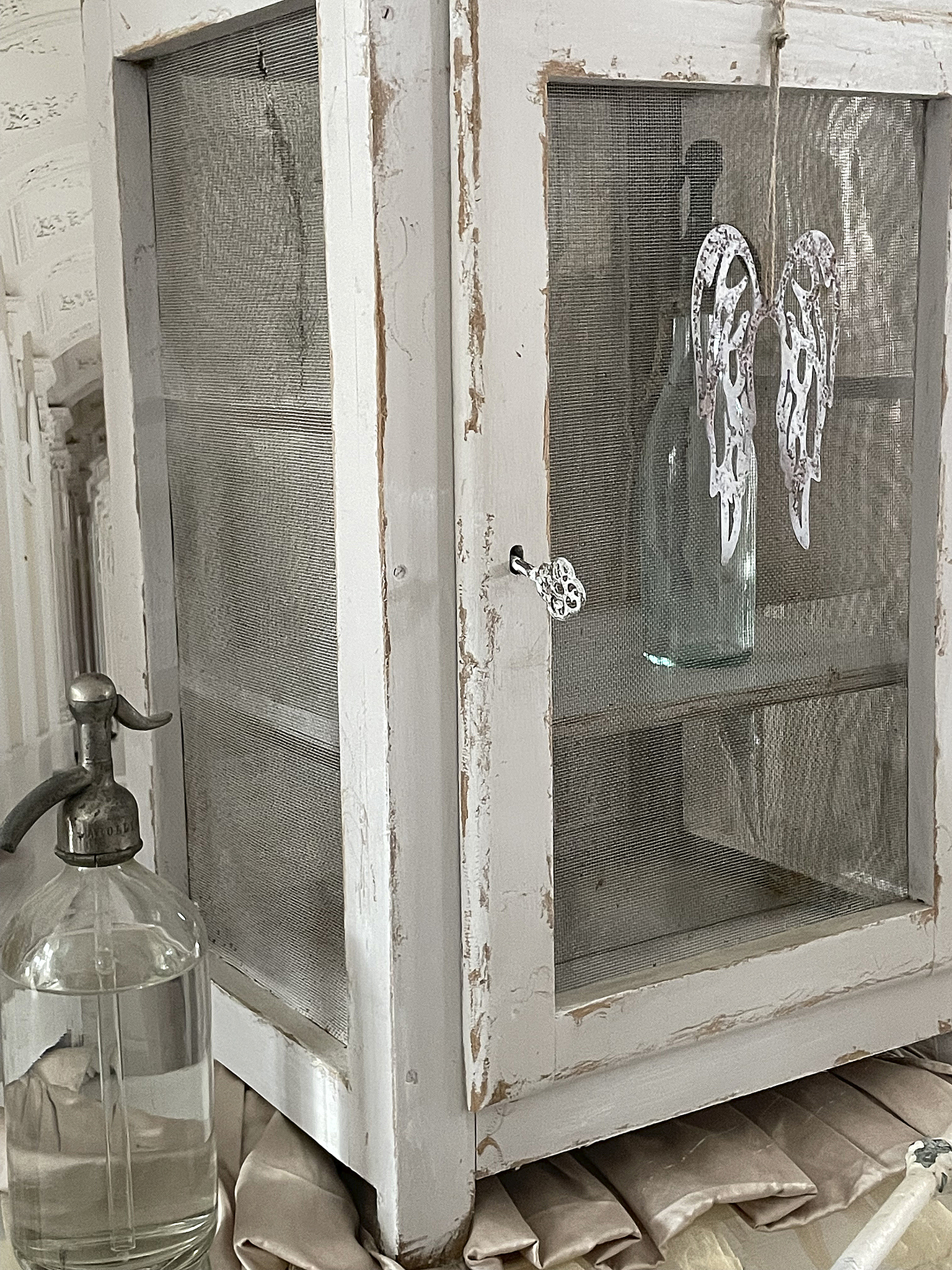 Vintage Glaskasten mit dekorativen Elementen Ein weißer vintage Glaskasten mit einem Glasflasche und dekorativen Flügeln im Inneren