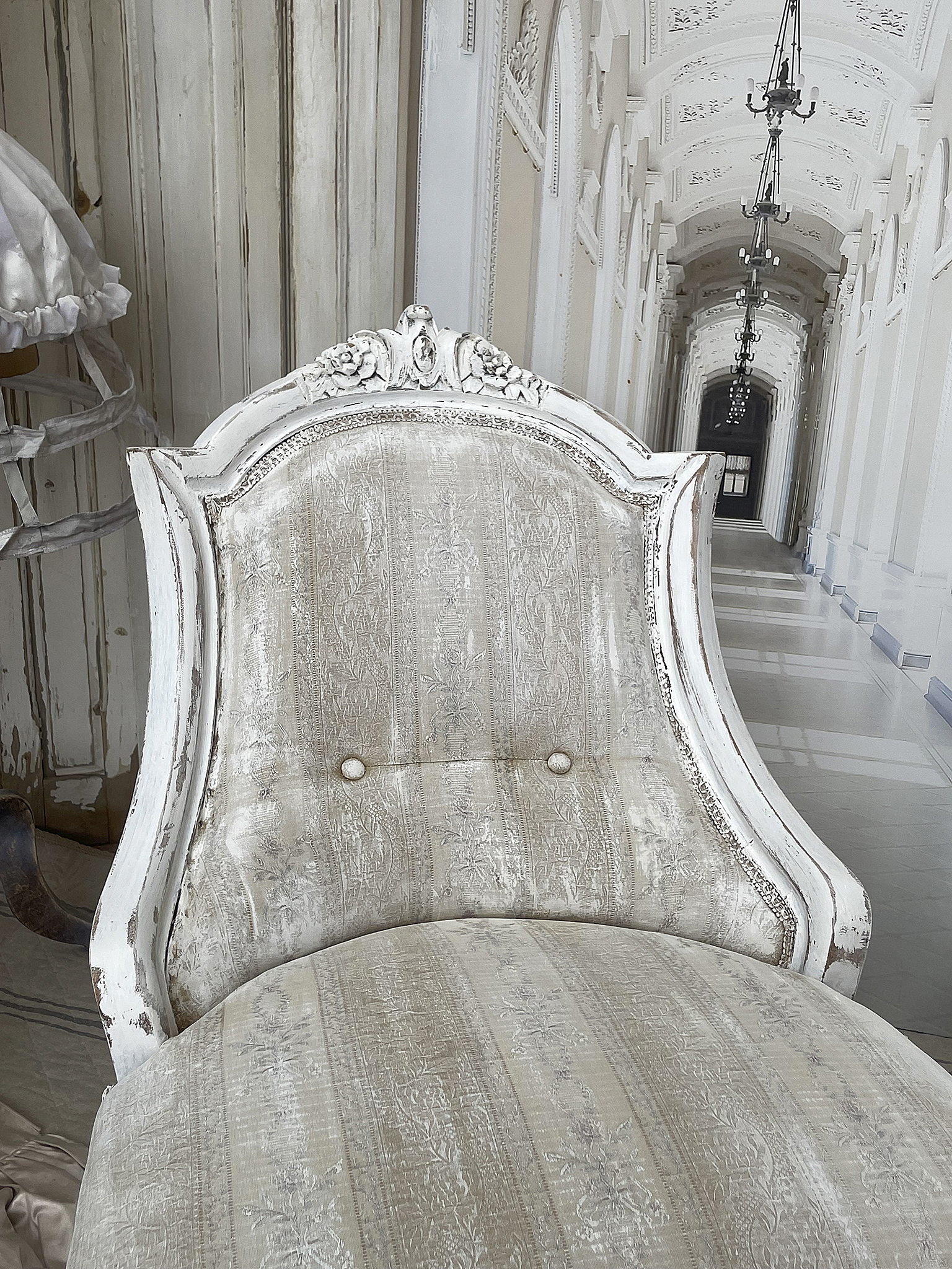 Eleganter Vintage-Sessel mit weißem Holzrahmen und zartem Stoffbezug Ein Vintage-Sessel in einem hellen Raum mit einem weißen Holzrahmen und einem feinen, bestickten Stoffbezug.