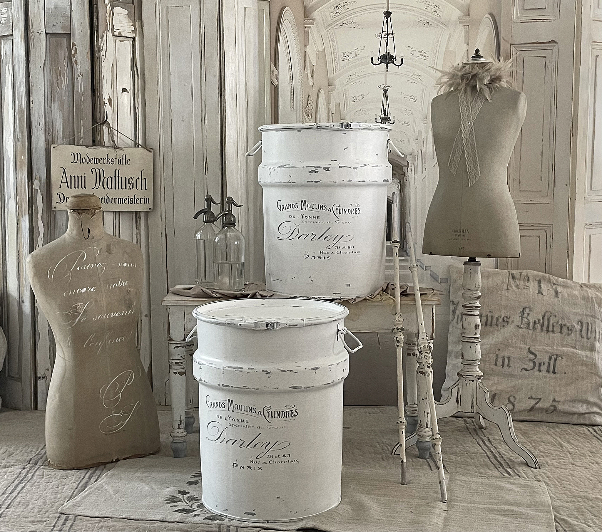 Ein elegantes Arrangement aus antiken Mannequins, weißen Eimern und nostalgischen Dekorationsgegenständen in einem stilvollen Raum.