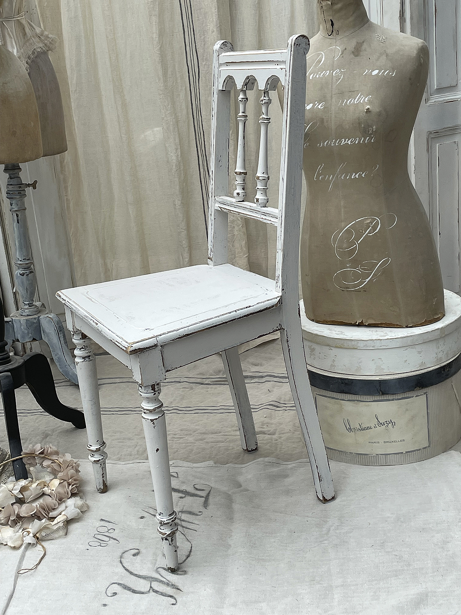 Antiker weißer Stuhl mit Mannequin im Vintage-Stil Weißer Vintage-Stuhl neben einem Mannequin in einem shabby-chic Ambiente
