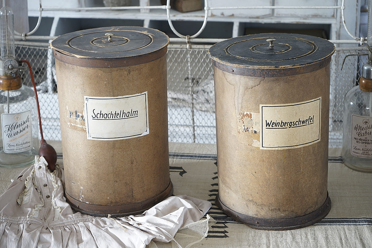 Antike Behälter beschriftet mit Schachtelhalm und Weinbergsulf auf einem Tisch.
