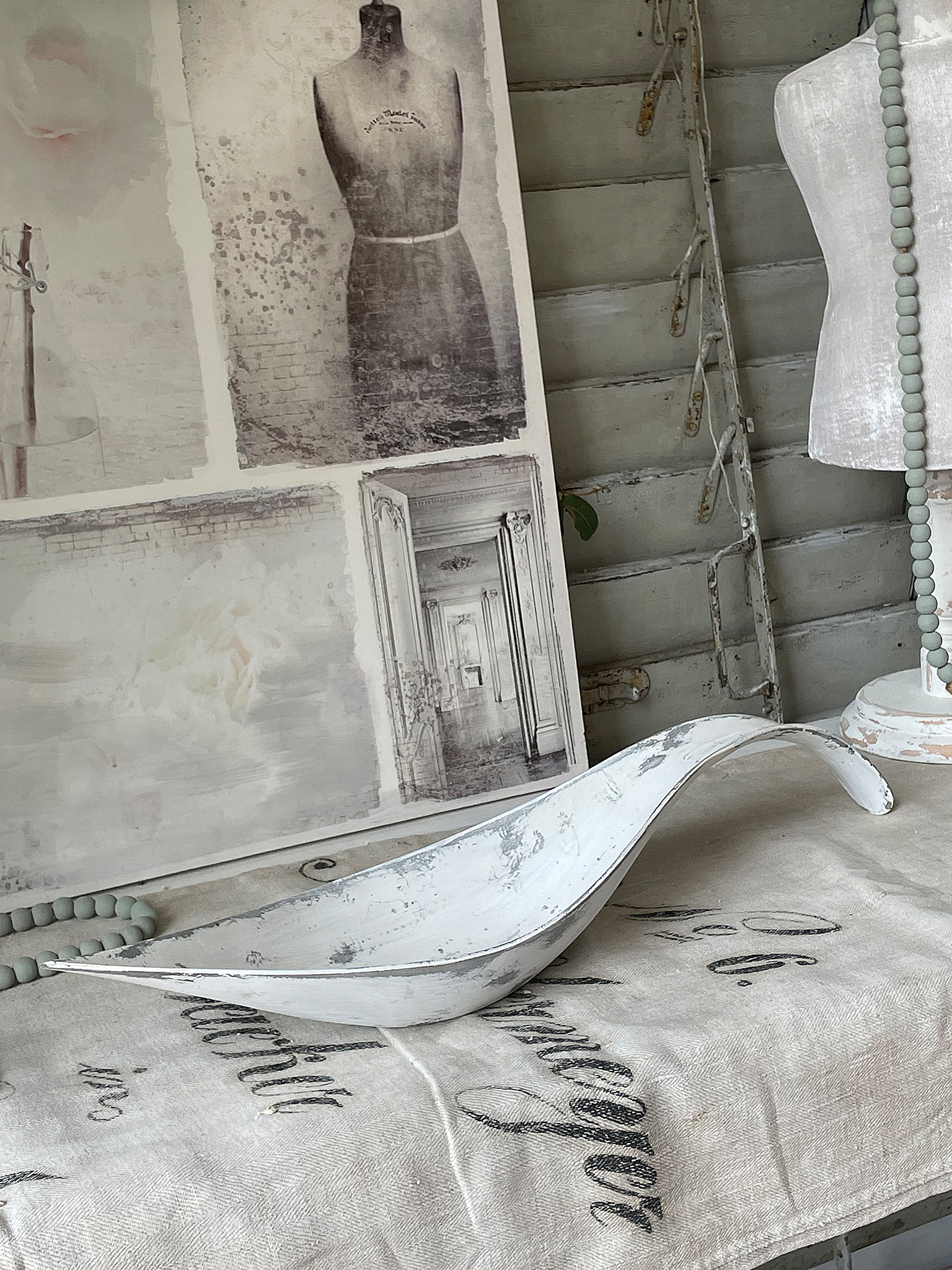 Dekorative weiße Schale auf einem Tisch mit vintage Stoff Weiße dekorative Schale auf einem Tisch, umgeben von stilvollem Interieur und Bildern