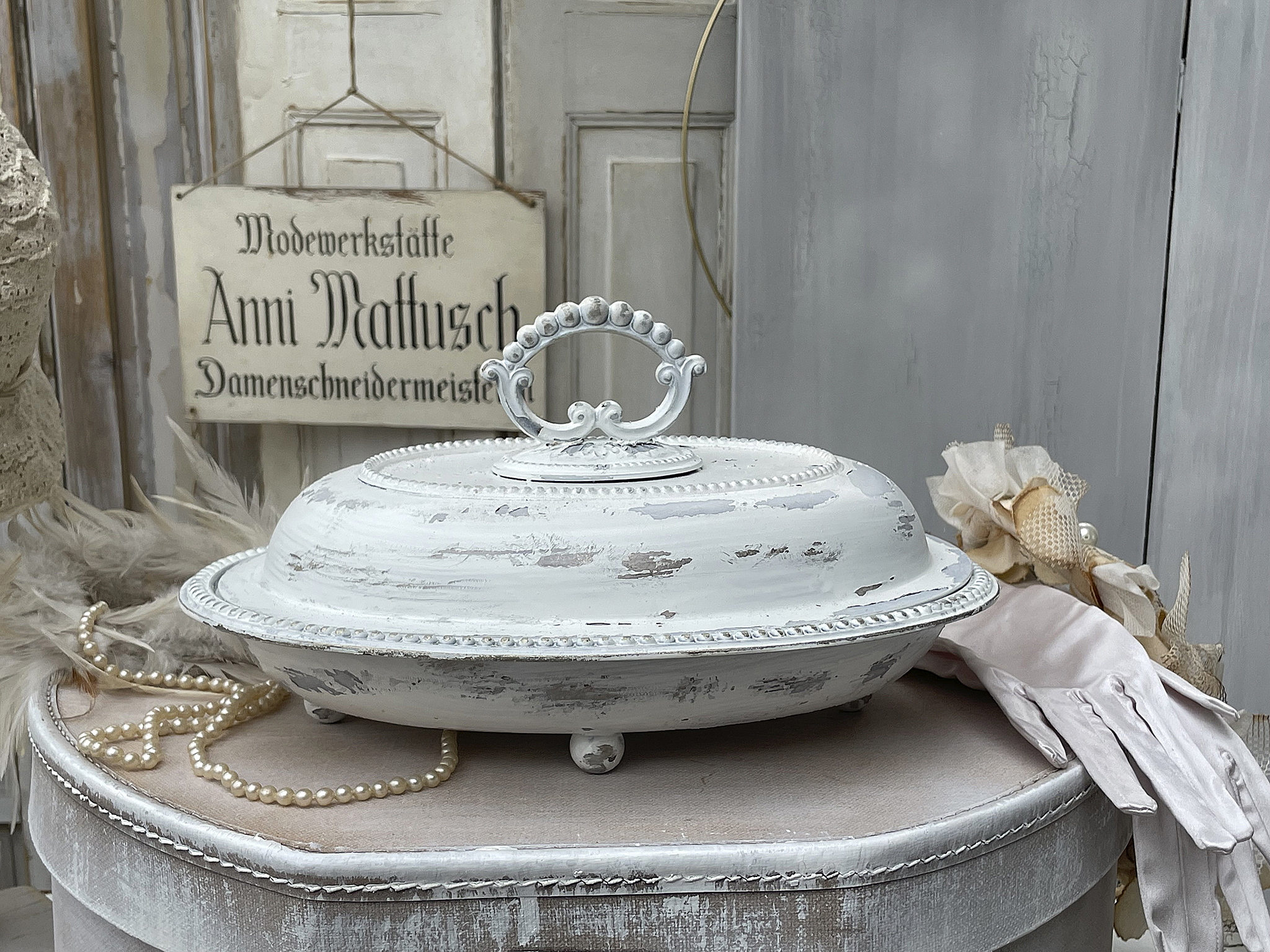 Elegante vintage Servierplatte aus Porzellan mit Deckel Weiß lackierte Servierplatte mit nostalgischem Design, verziert mit Perlen und einem Deckel, auf einem runden Tisch mit Zubehör.
