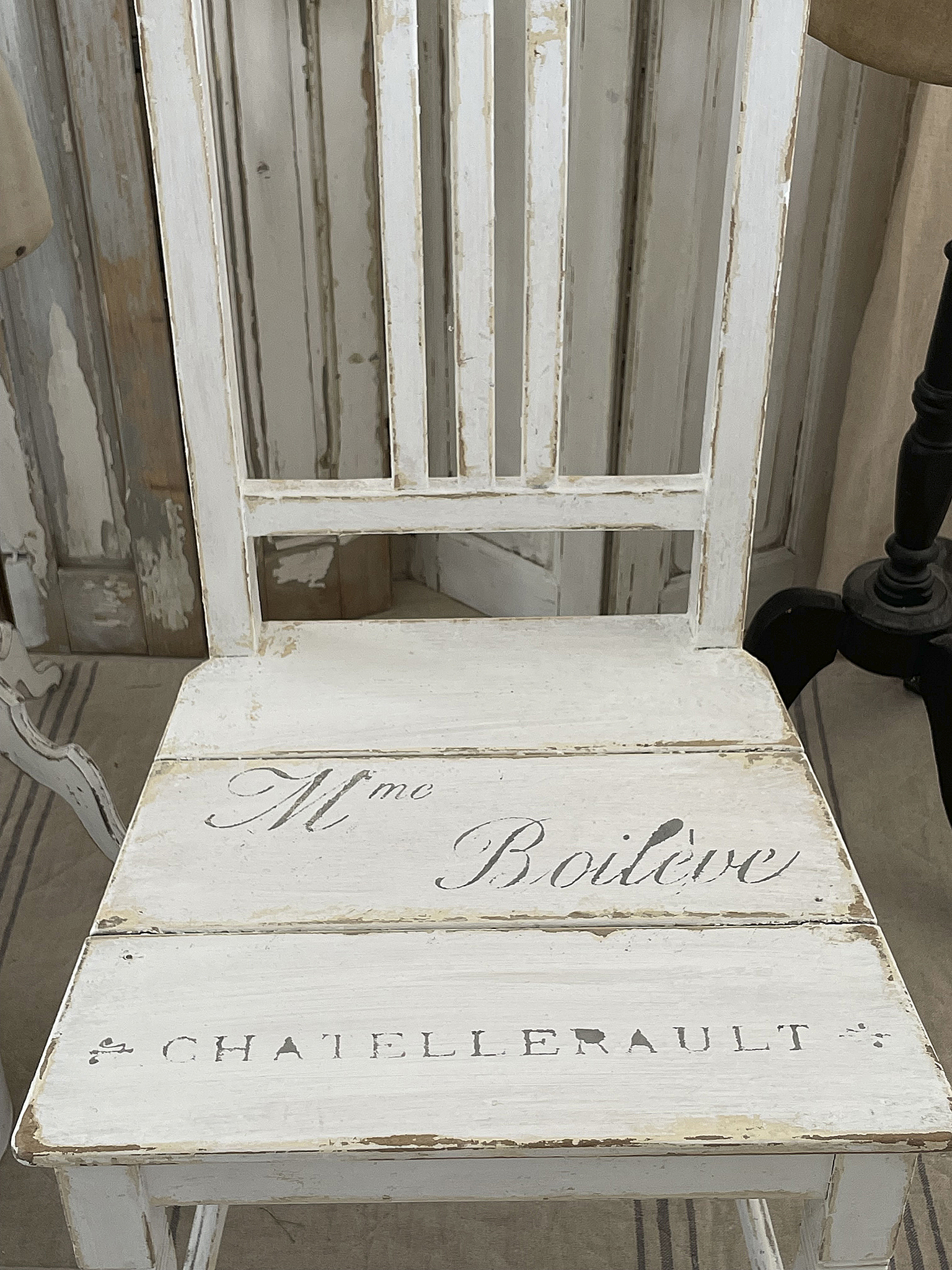 Vintage Stuhl mit französischem Schriftzug Weißer Vintage-Stuhl mit der Aufschrift 'Mme Boilève CHATELETAULT' auf der Sitzfläche.