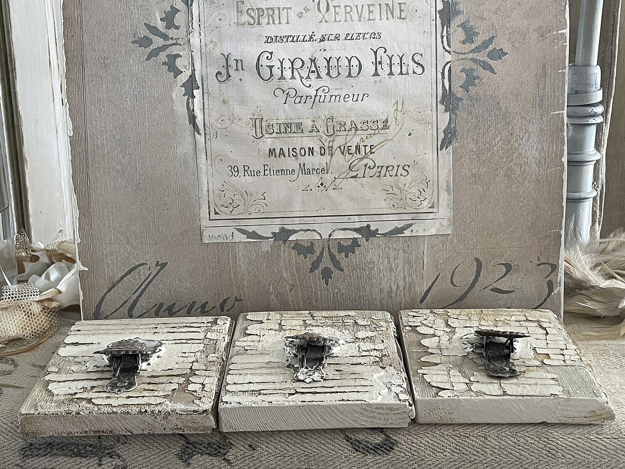 Drei rustikale Aufbewahrungskästen mit Metallverschluss und vintage-ähnlicher Oberflächenbehandlung, im Hintergrund ein nostalgisches Parfumetikett aus dem Jahr 1923.