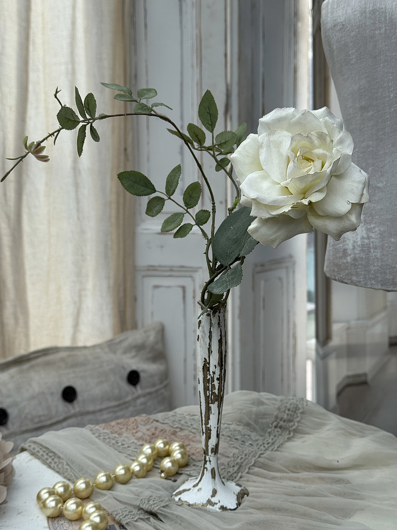 Edelweiß Rose in einer vintage Vase mit Perlenkette Eine elegante Edelweiß Rose in einer antiken Vase, umgeben von einer Perlenkette auf einem Tisch.