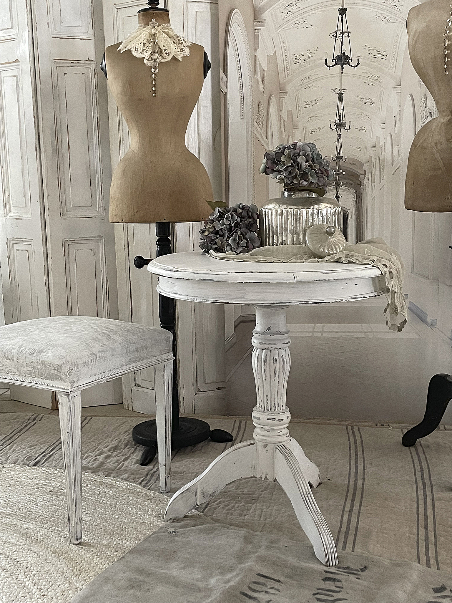 Eleganter runder Tisch mit vintage Stil und Dekoration Stilvoller weißer Tisch mit Dekoration, umgeben von Mannequins und elegantem Interieur