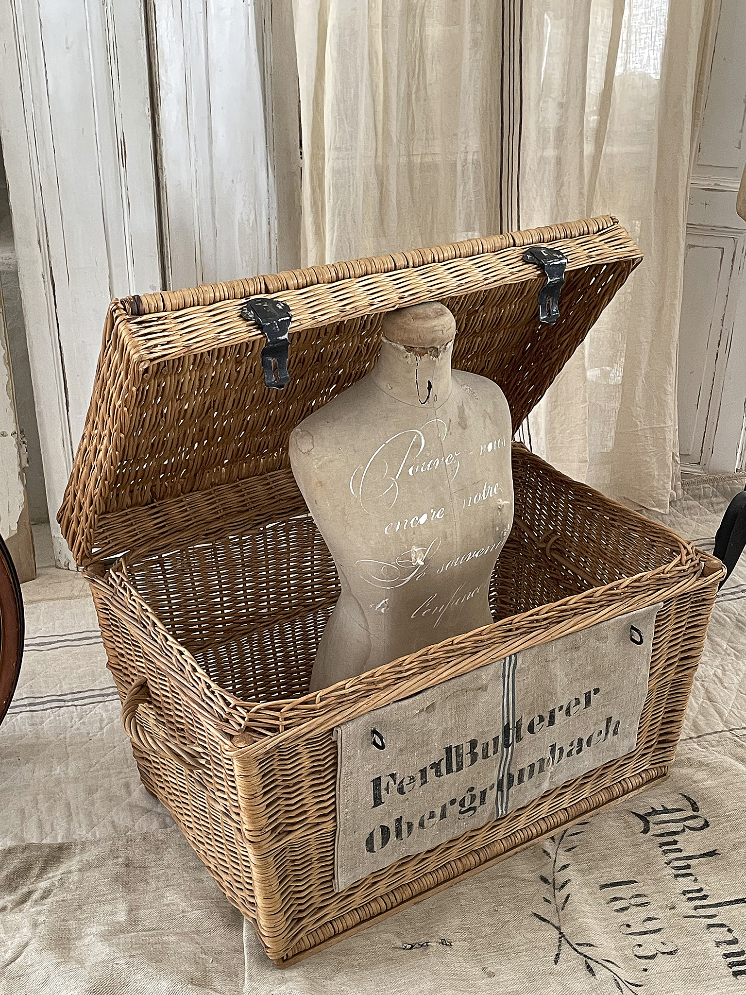 Antiker Wäschekorb mit Schaufensterpuppe im Vintage-Stil Wäschekorb aus Weide mit offenem Deckel und einer Schaufensterpuppe darin, rustikale Dekoration