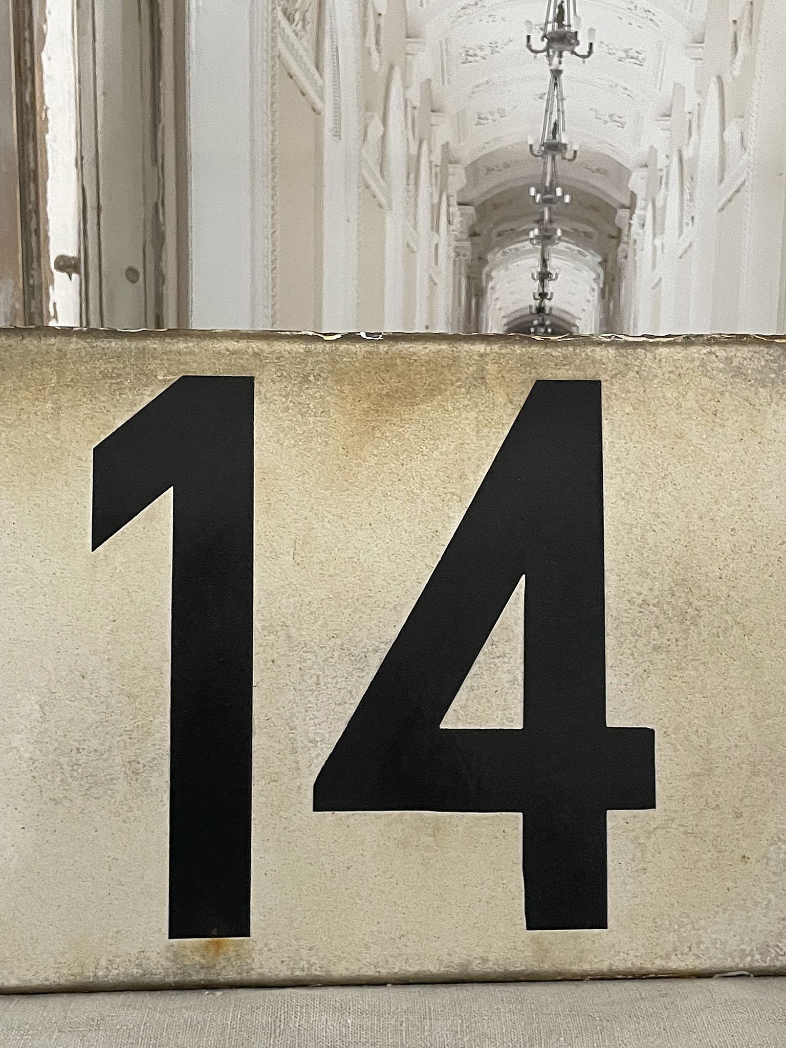 Helles Schild mit der Zahl 14 in schwarzer Schrift, im Hintergrund ein heller Flur