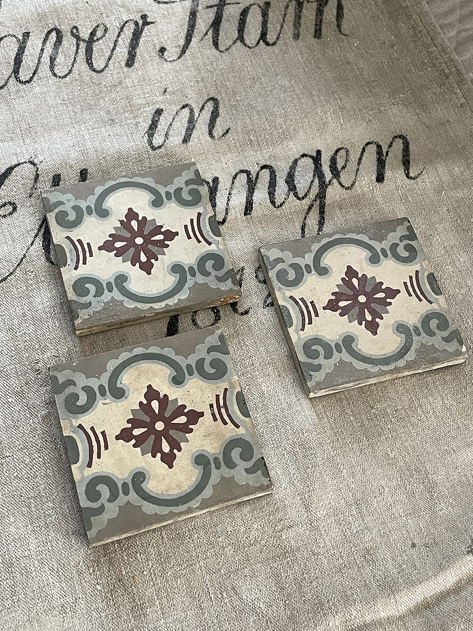 Drei bunte, dekorative Fliesen im Vintage-Stil liegen auf einer neutralen Stoffunterlage.